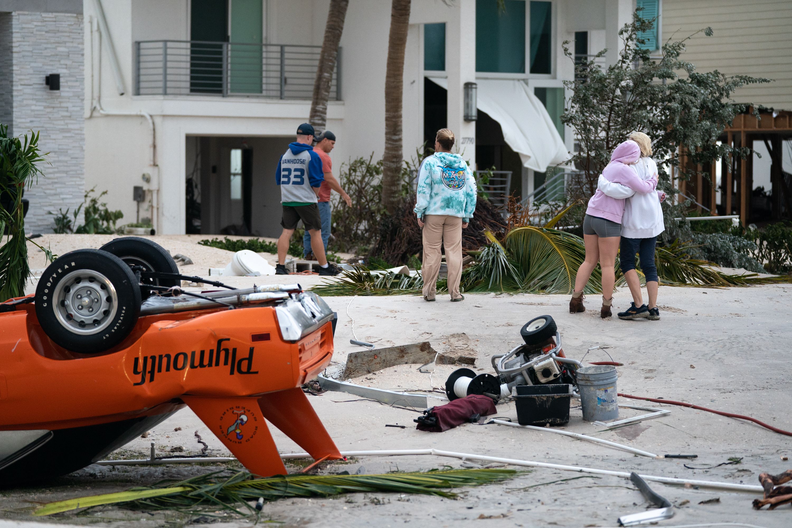 people standing around hurricane debris and a damaged car