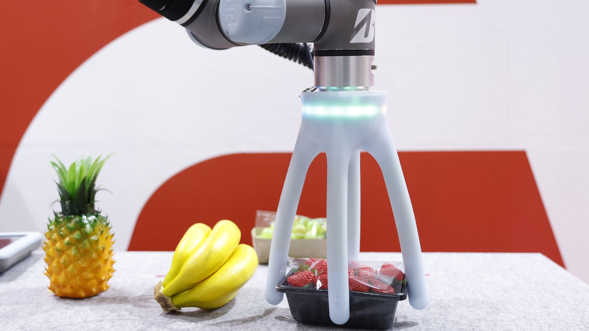 A soft robotic hand grips a container of strawberries