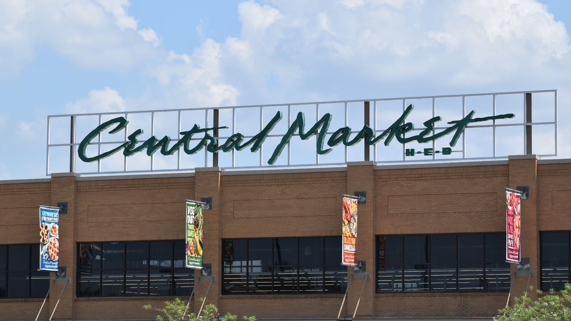 A Central Market grocery store sign against a blue sky with clouds.