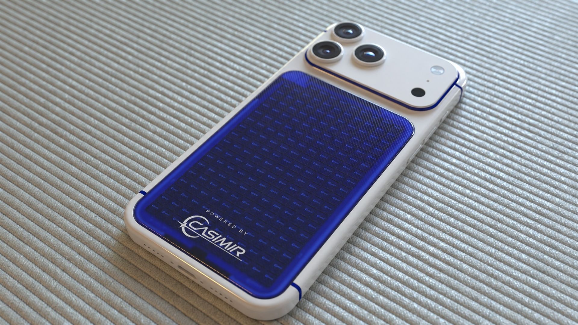 White smartphone with a blue, textured back panel and a triple-camera module rests on a light ribbed fabric surface; white case with blue accents adds a glossy finish.