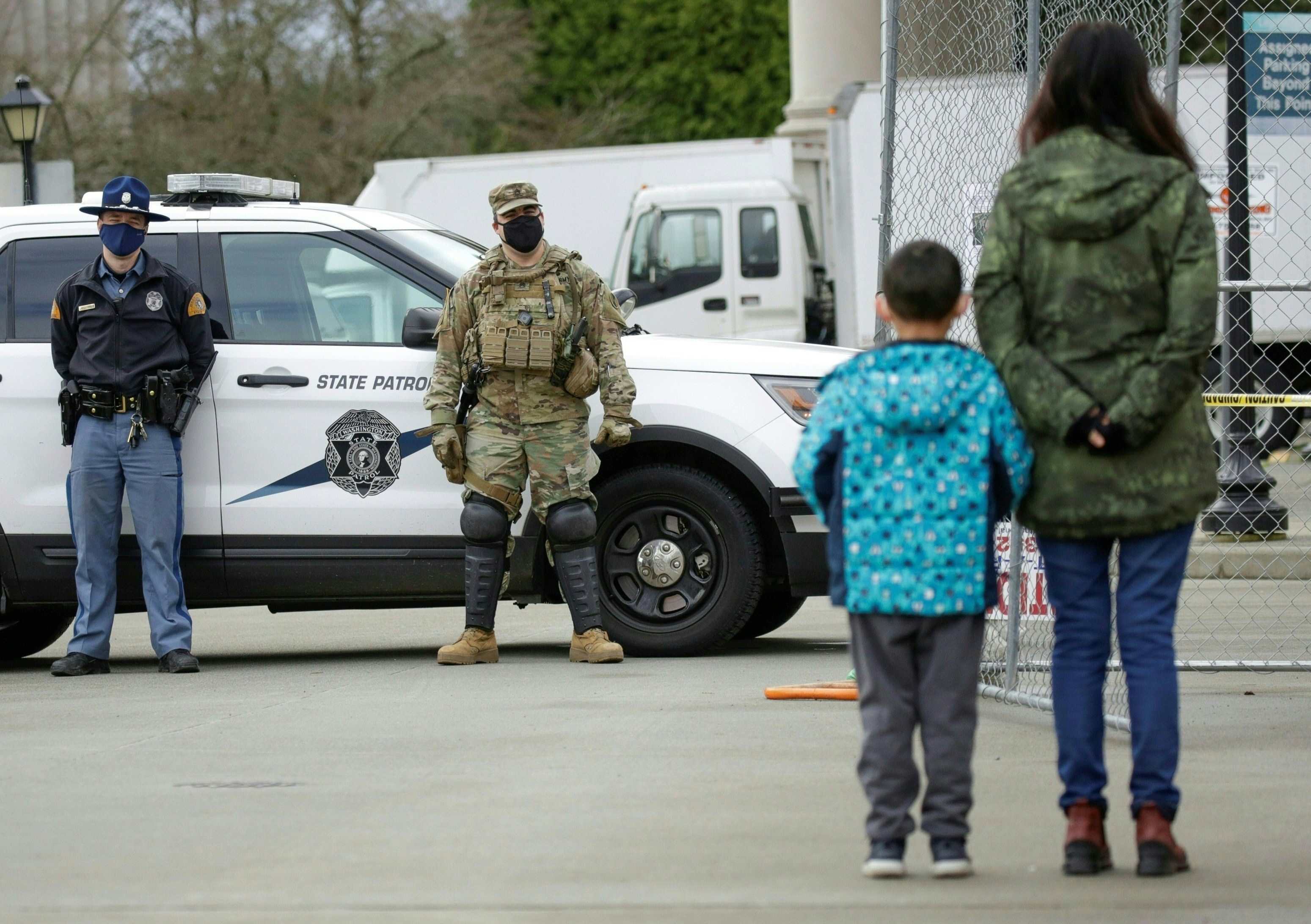A woman and child look on as members of the Washington National Guard and State Police stand outside the state Capitol in Olympia, Washington on January 17
