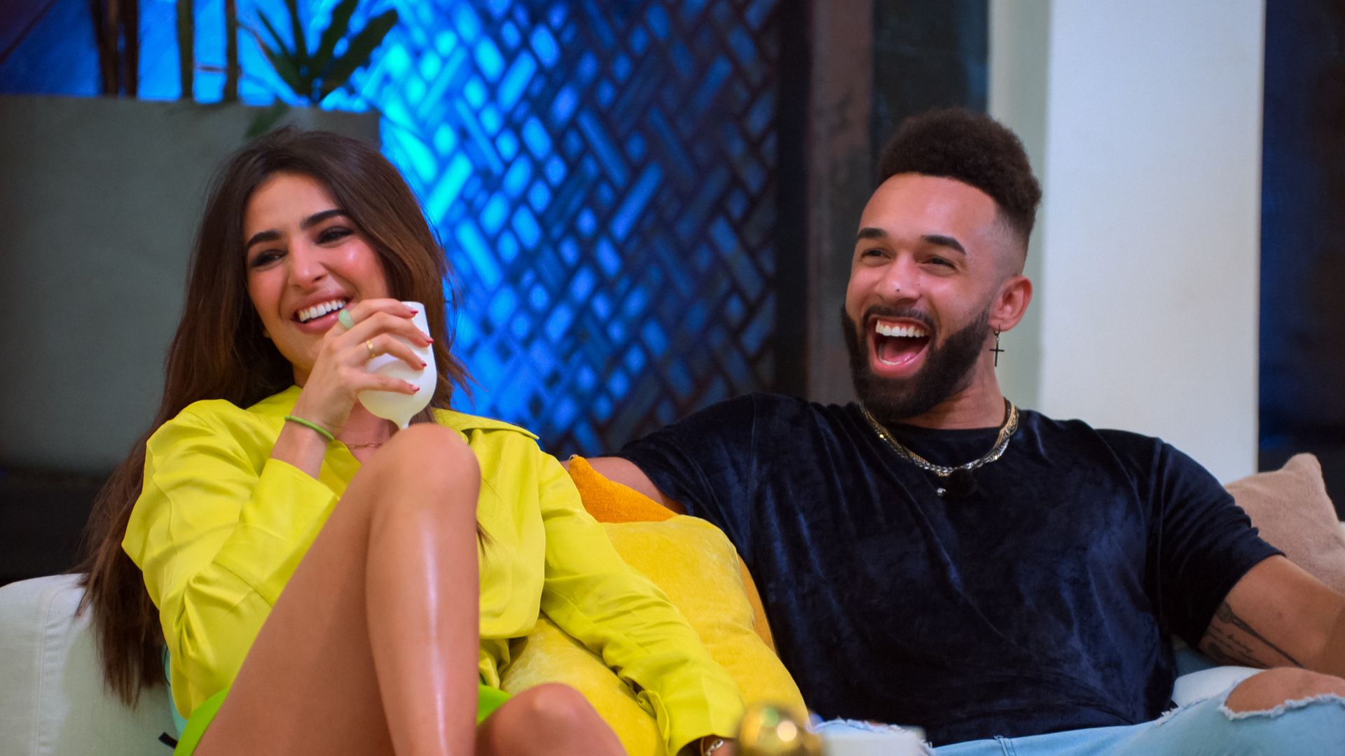 Two attractive people sitting on a couch, laughing at the funniest thing ever said