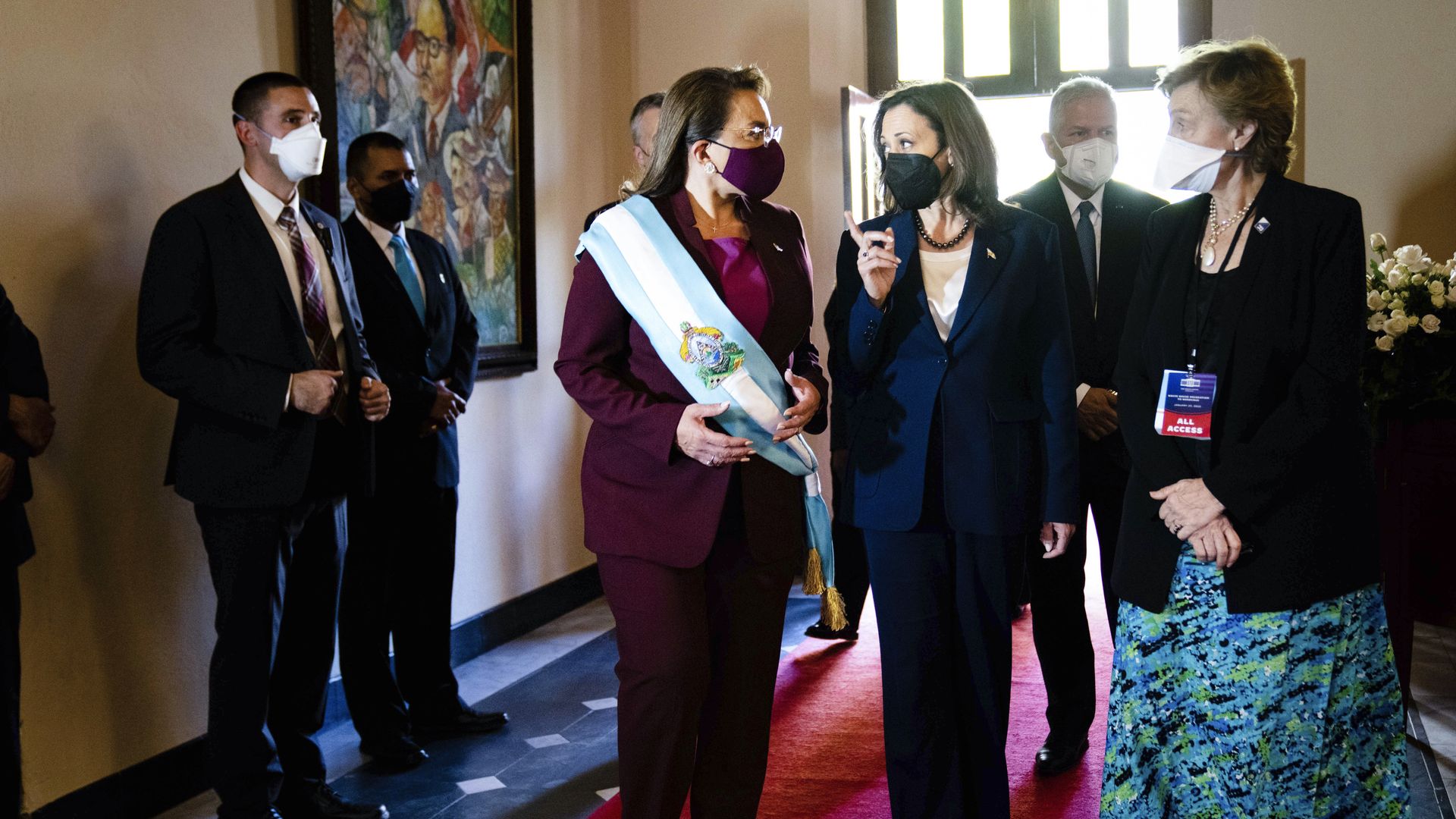 Photo of a masked Kamala Harris and Xiomara Castro walking in a hall while speaking, with aides trailing behind them
