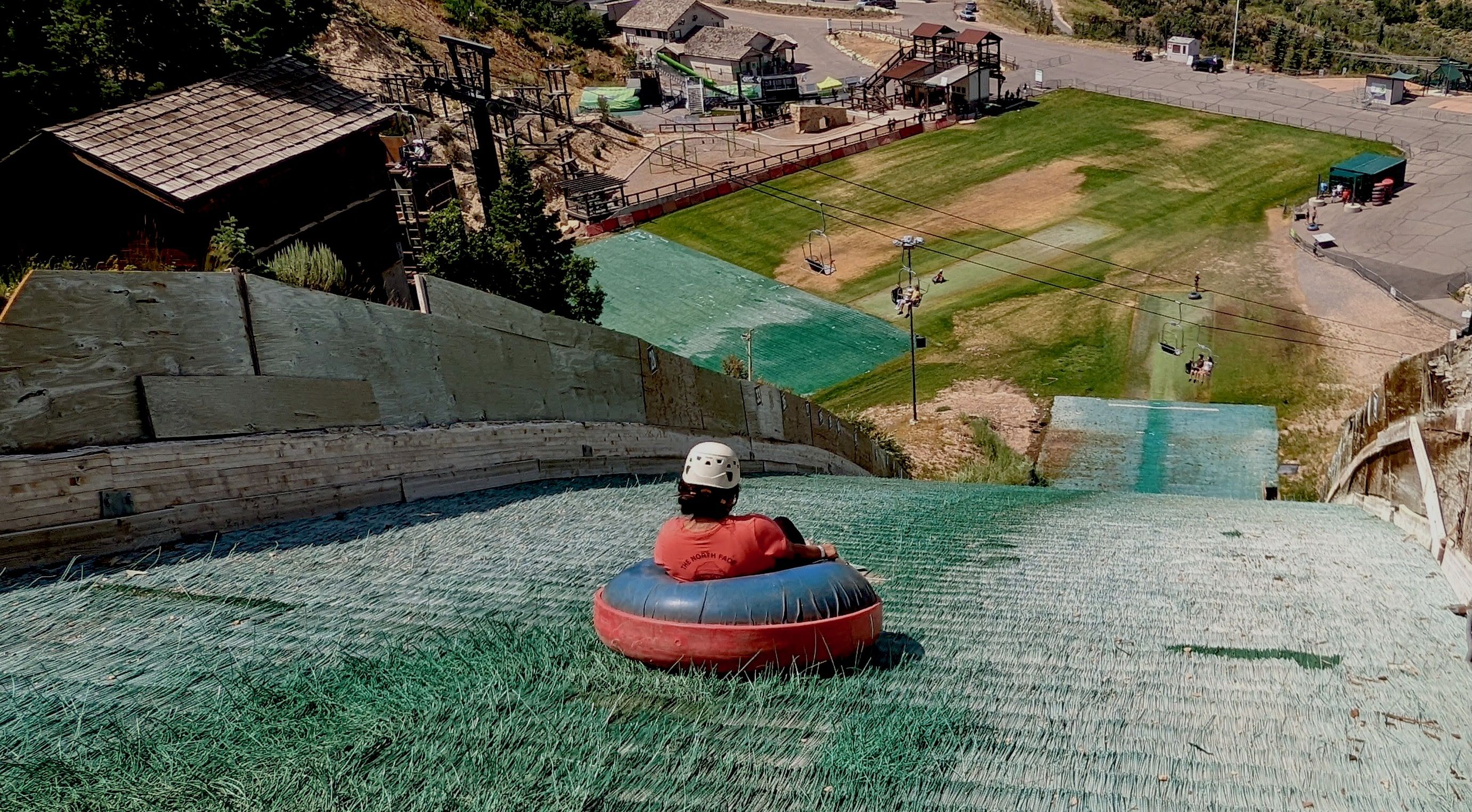 A woman in an innertube heads down a steep slope on wet fake grass.