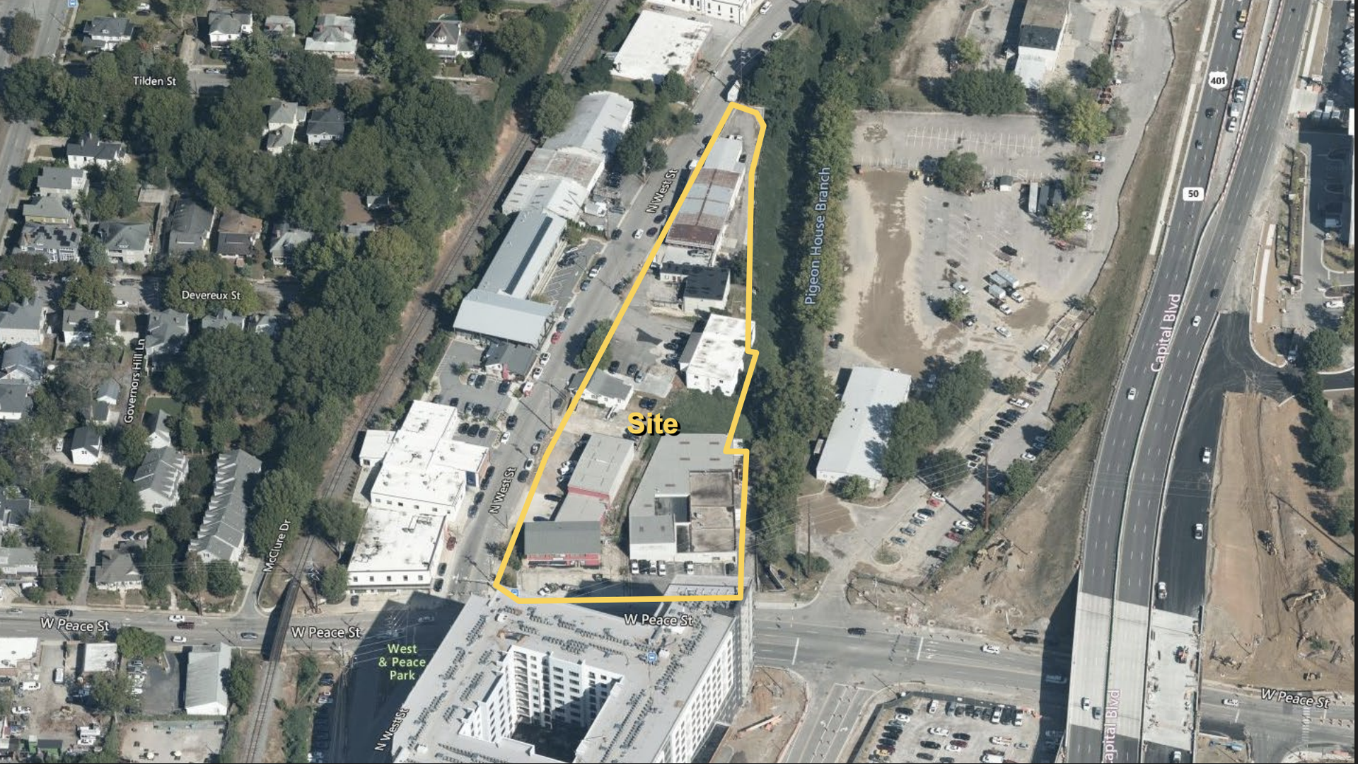 Aerial view of an urban area with a yellow outline marking a site near W Peace St, N West St, and Capital Blvd, surrounded by buildings, parking lots, roads, and greenery.