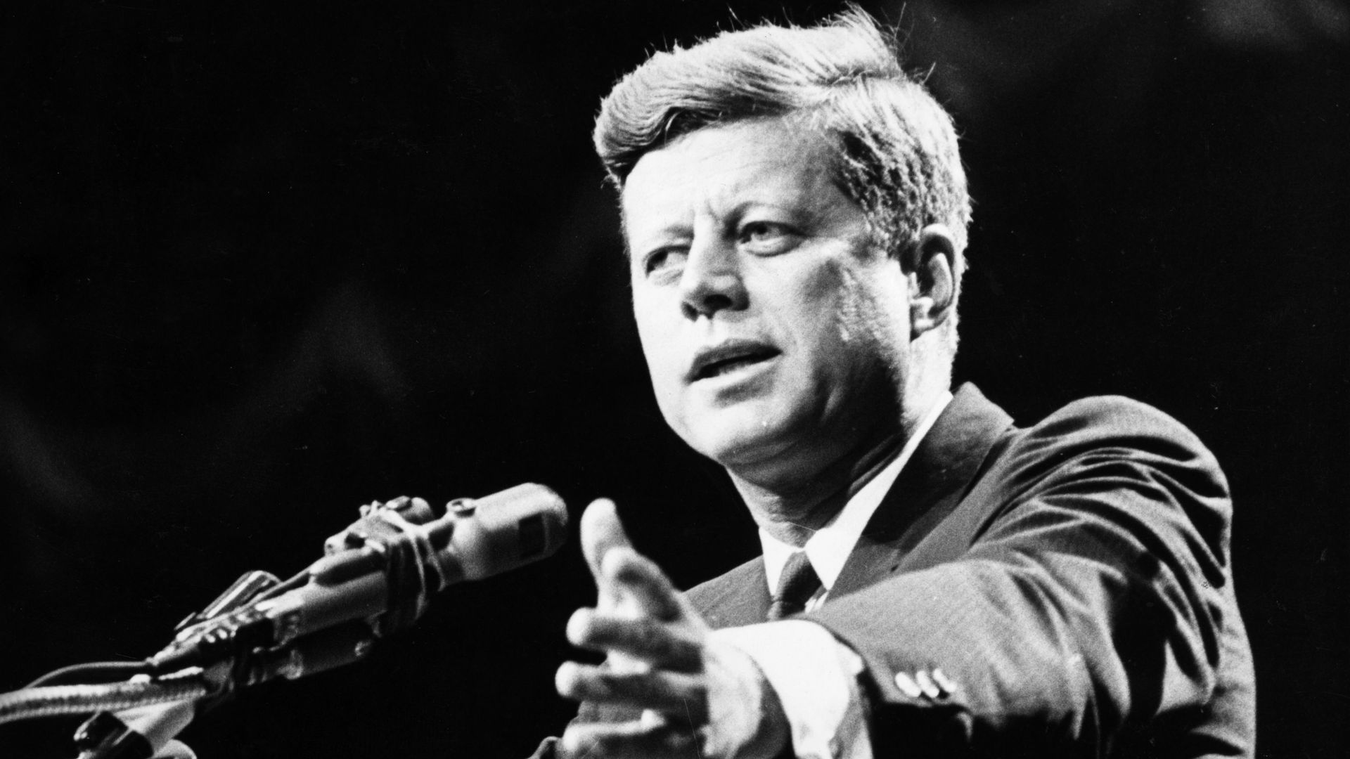 Former United States President John F. Kennedy standing in front of a microphone.