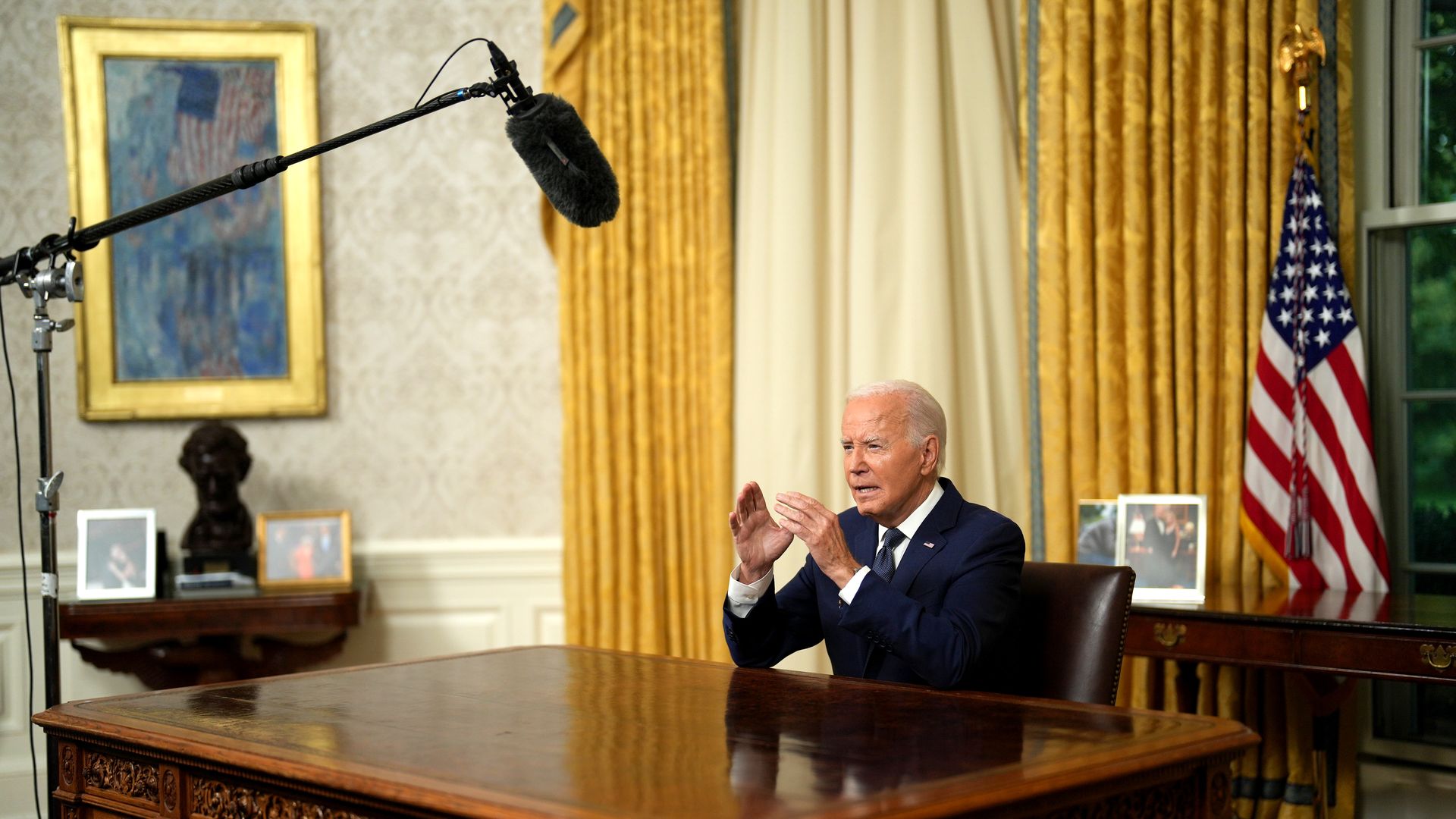 President Biden speaks behind his Oval Office Desk with a boom microphone above him