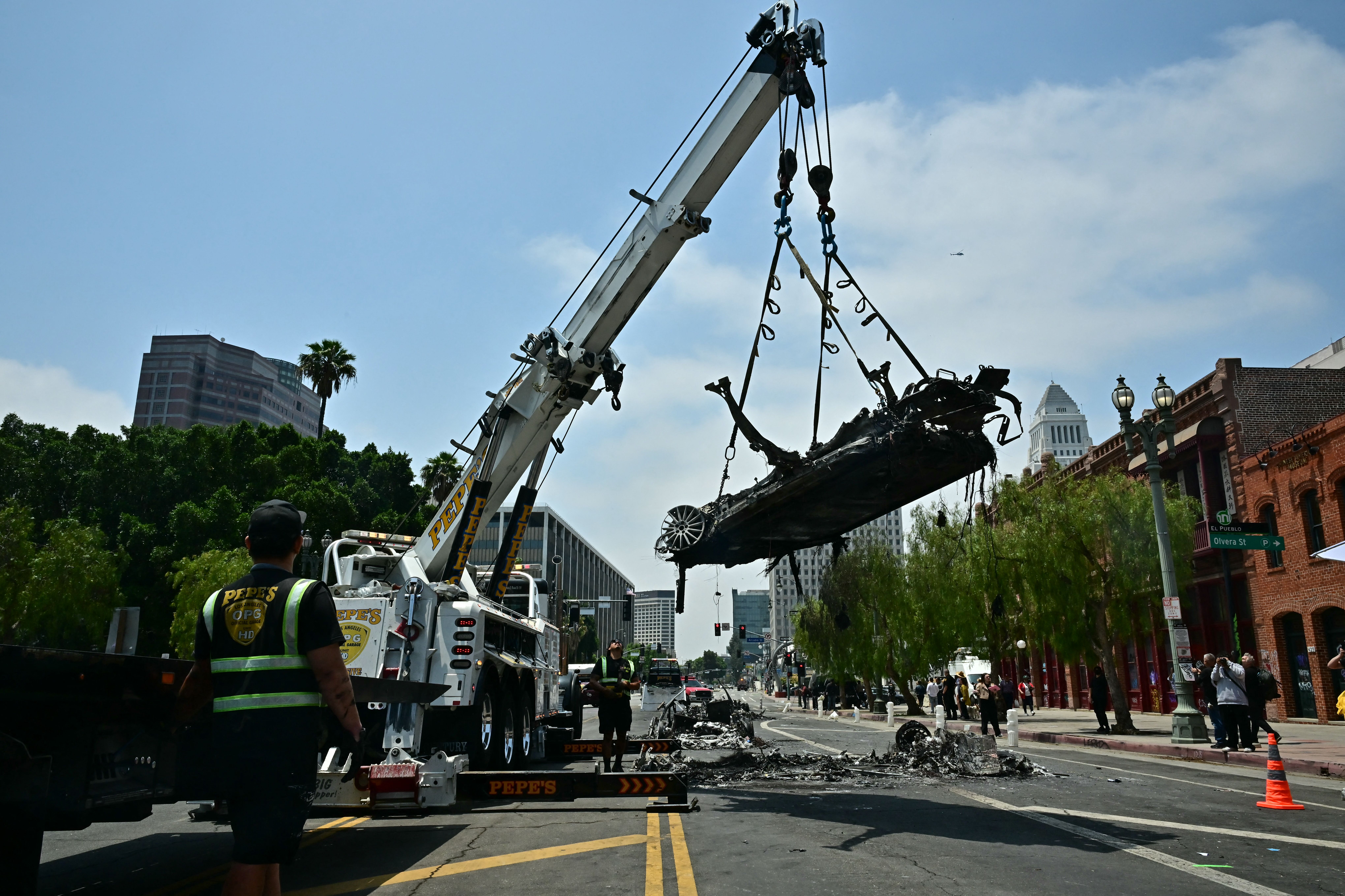 Workers remove a charred Waymo self-driving car yesterday that was burned during protests in downtown L.A.