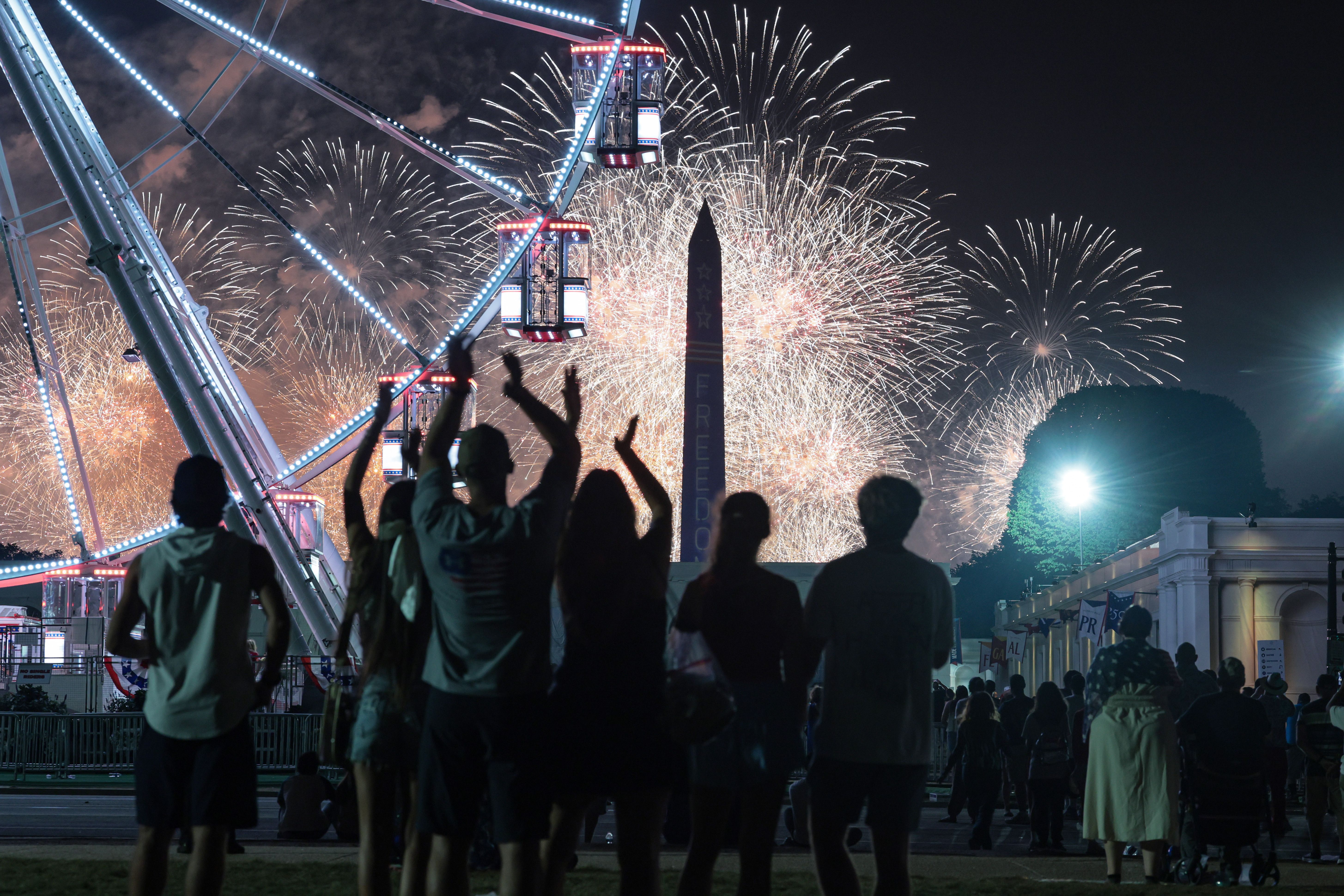 Silhouetted spectators watch fireworks erupt behind a Ferris wheel and a Washington Monument replica on the National Mall during the Salute to America 250 celebration in Washington, D.C., on July 4, 2026.