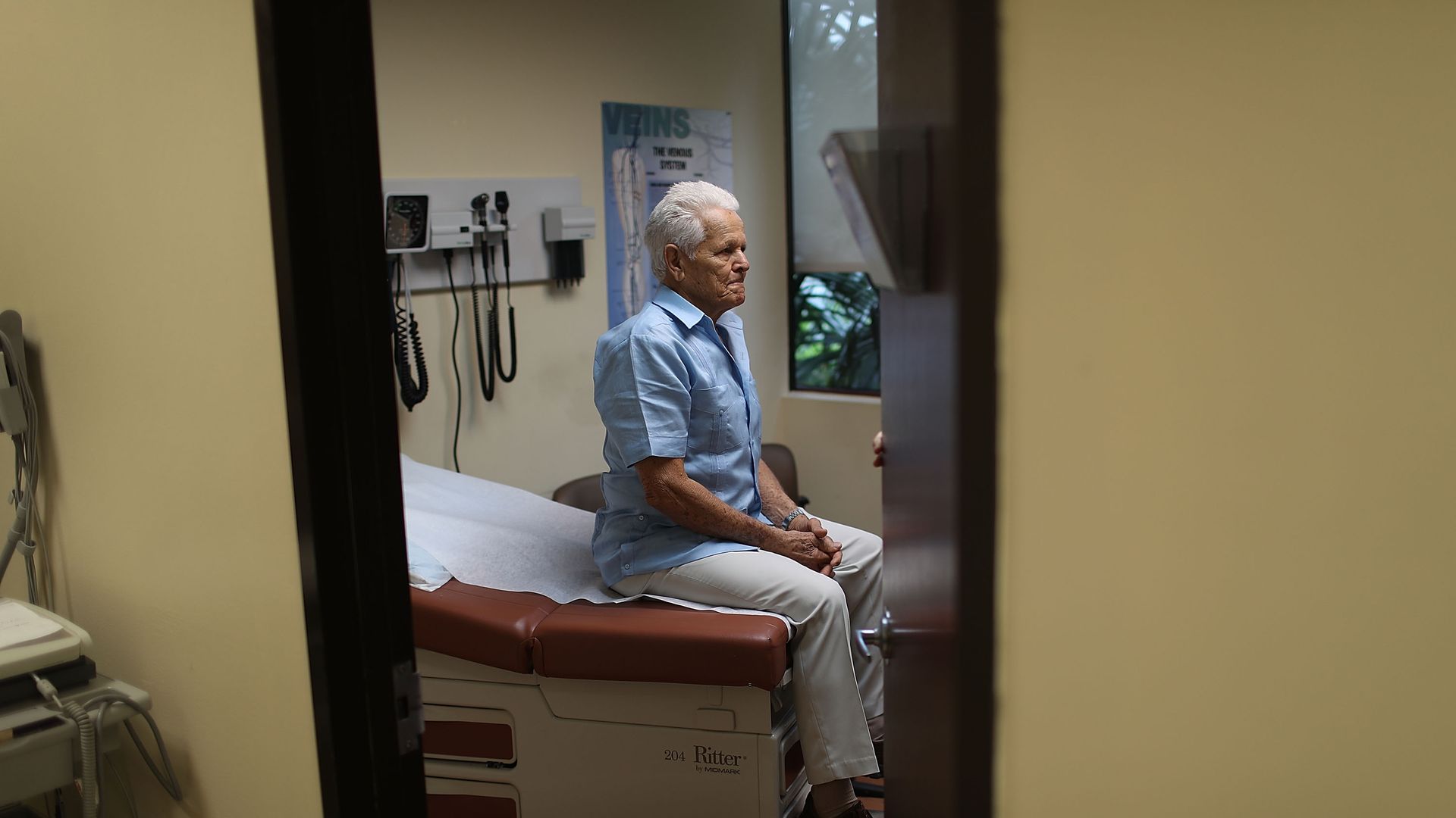 An elderly patients sits in a hospital exam room.