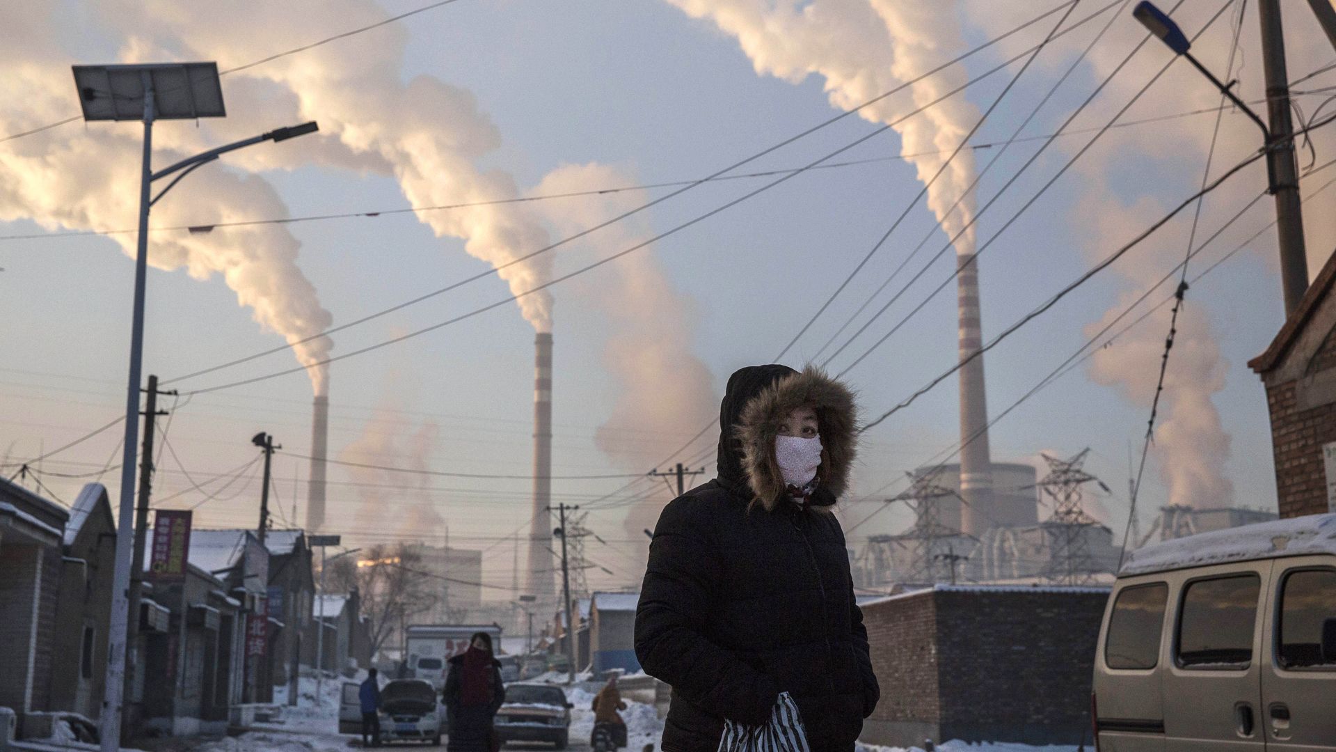 Smoke billows from stacks as a Chinese woman wears as mask while walking in a neighborhood next to a coal fired power plant on November 26, 2015 in Shanxi, China. 