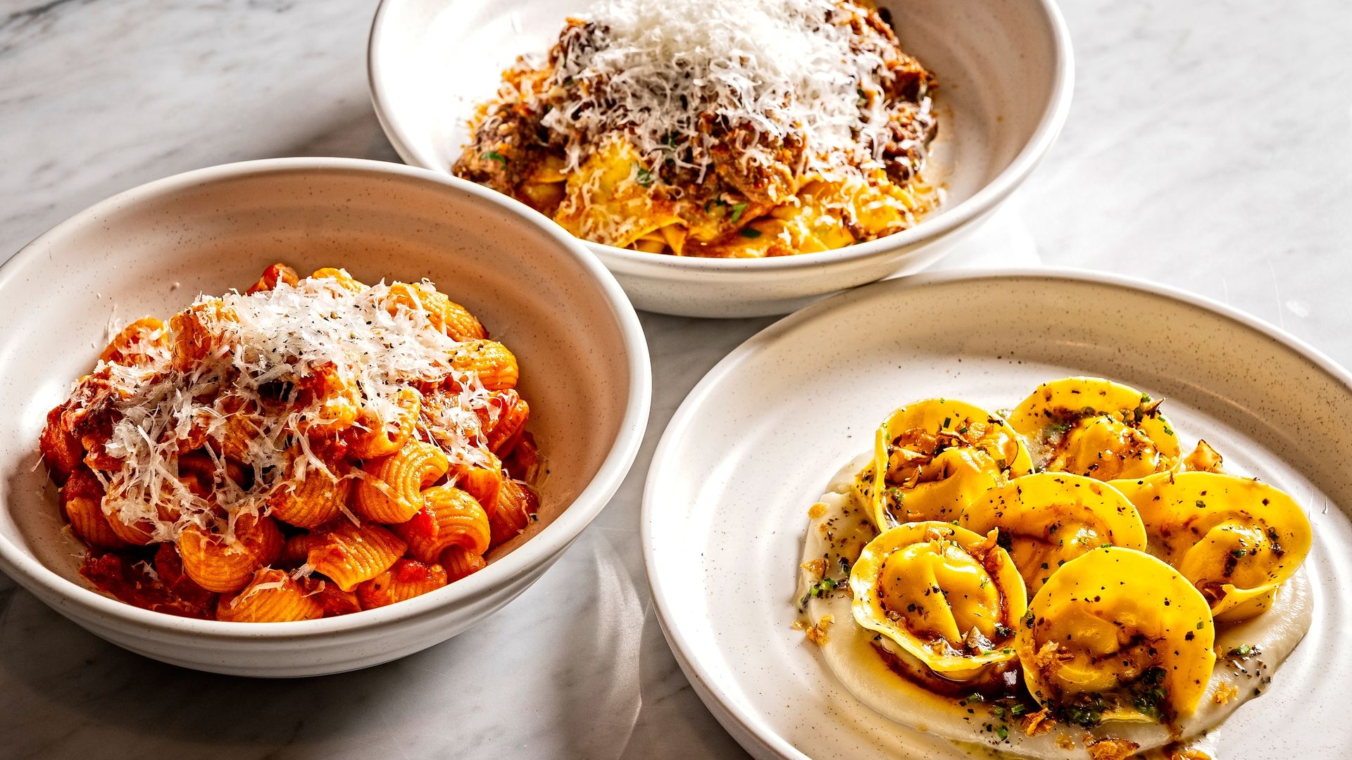 Three bowls of pasta, one red sauce amatriciana, another with meat ragu, and tortellini 
