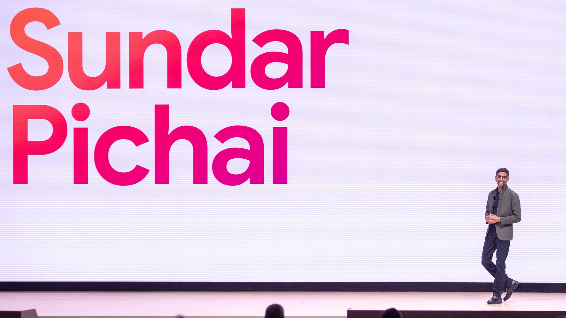 Sundar Pichai walks on a stage where a screen displays his name.