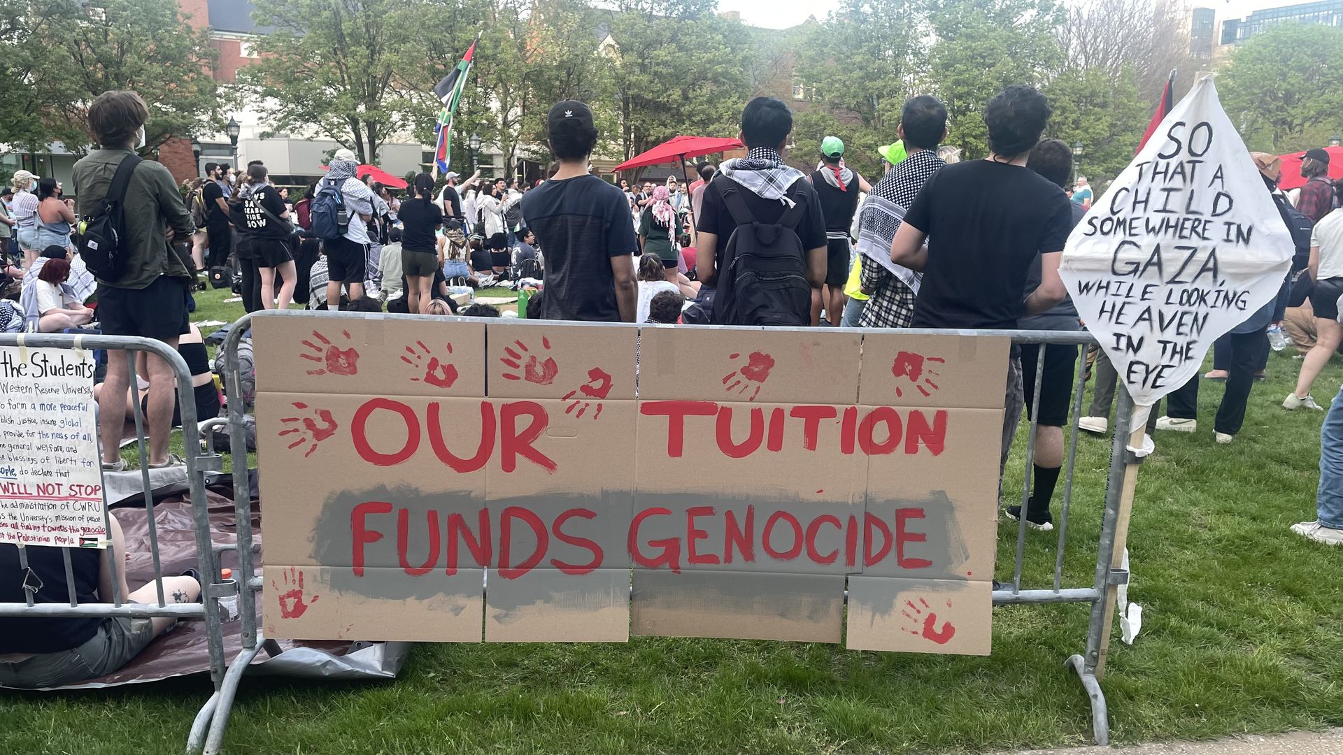 A sign reading "Our Tuition Funds Genocide" in red paint