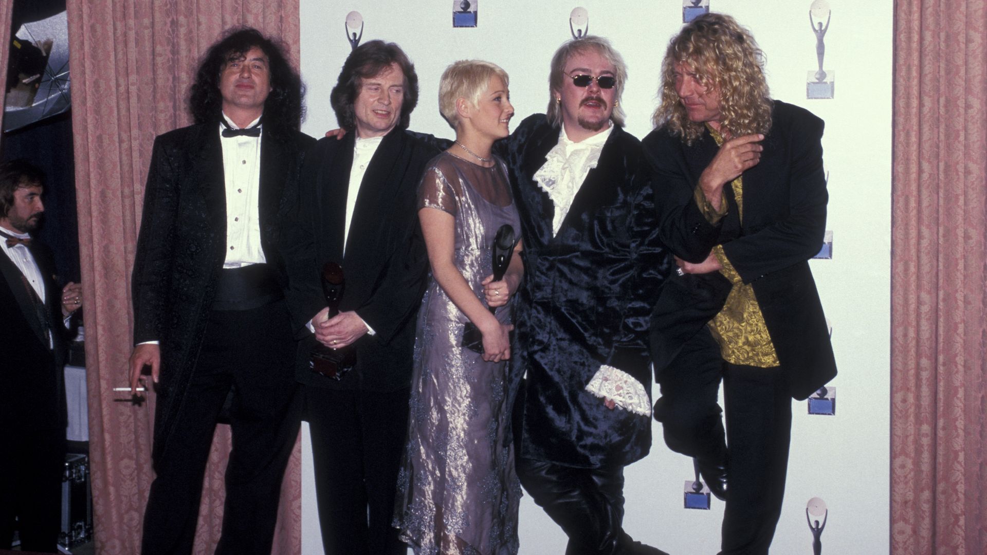 Jimmy Page, John Paul Jones, Zoe Bonham, Jason Bonham, and Robert Plant stand together on a red carpet.