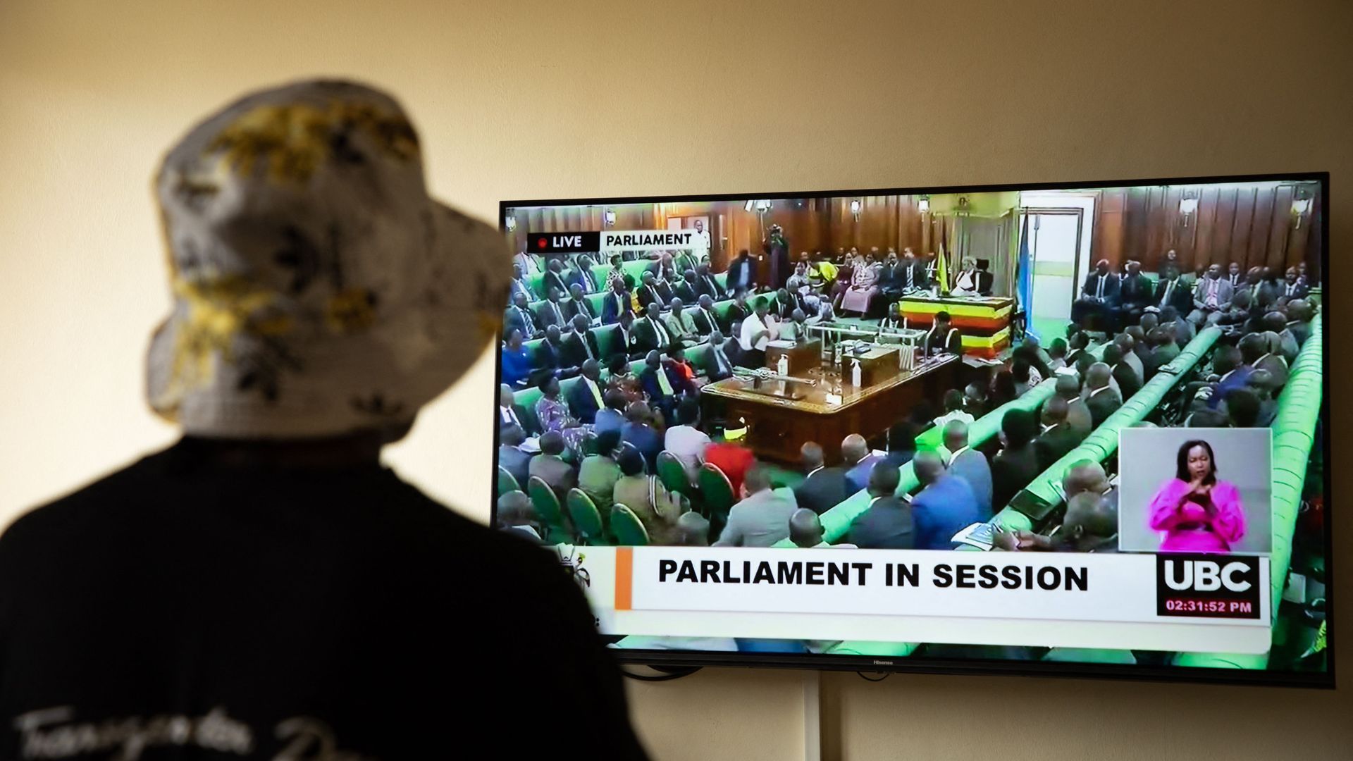 A Ugandan transgender woman who was recently attacked and currently being sheltered watches a TV screen showing the live broadcast of the session from the Parliament for the anti-gay bill