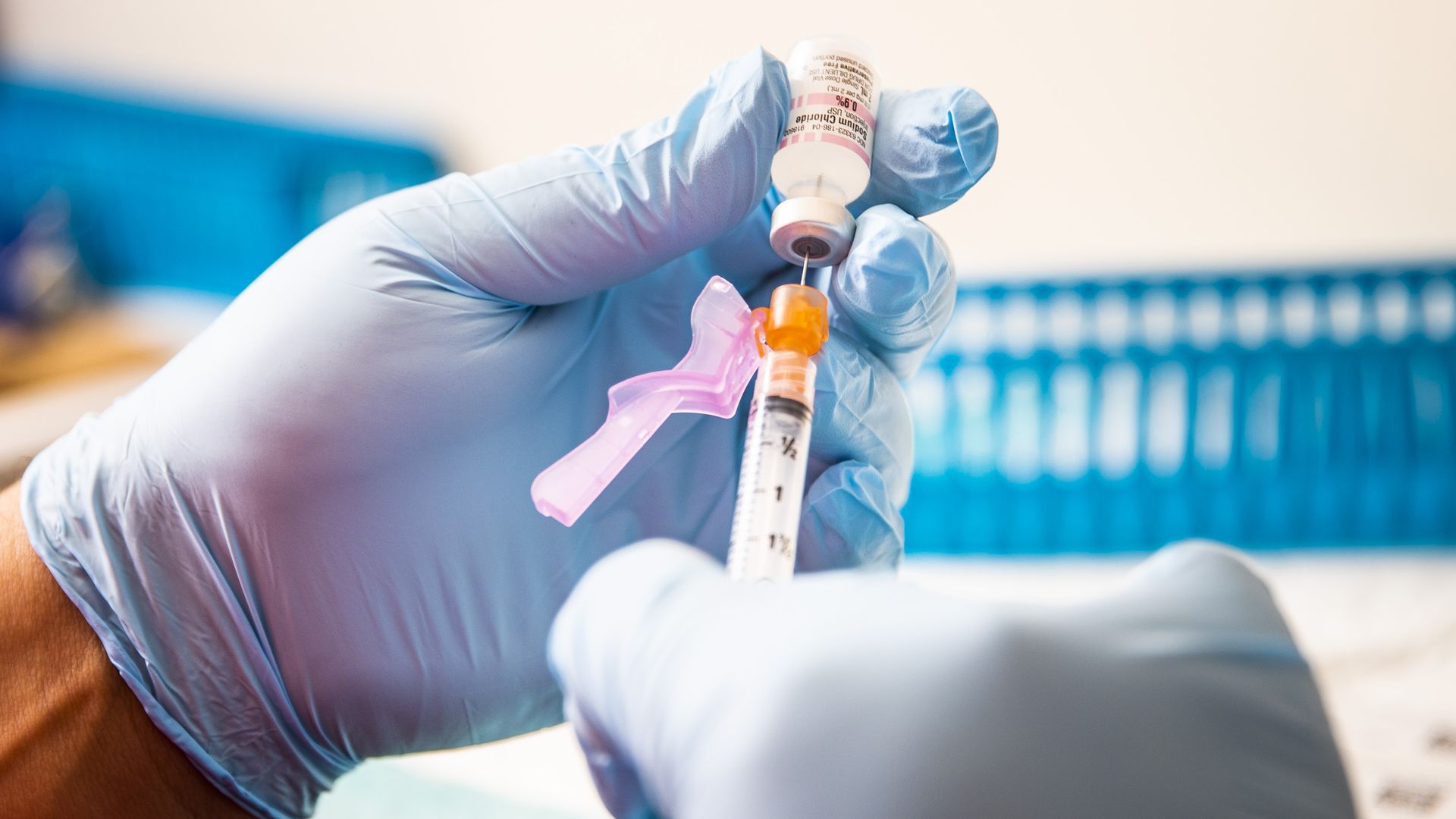 Photo of two gloved hands holding a syringe of the COVID vaccine