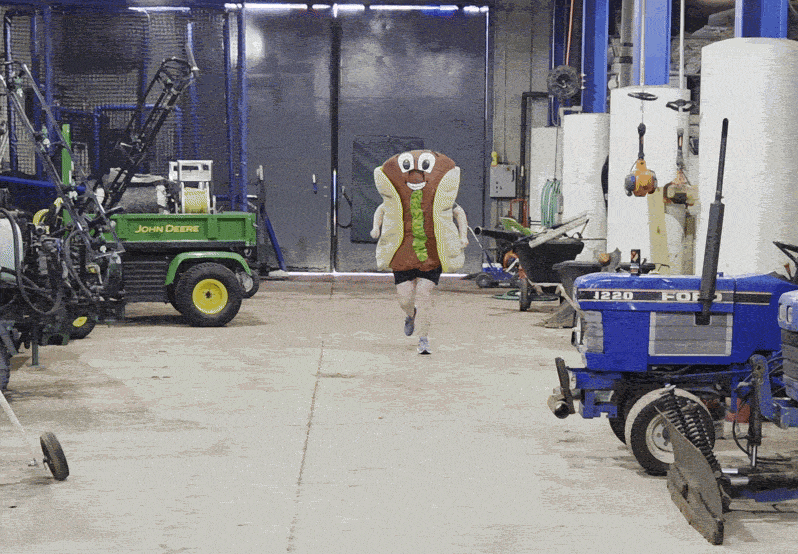 A gif of Alissa running toward the camera in a Rickey Relish hot dog mascot costume, behind the scenes at Huntington Park.