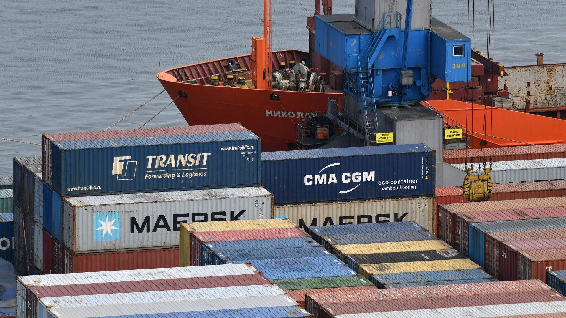 Photo of stacks of container shipments sitting next to a boat