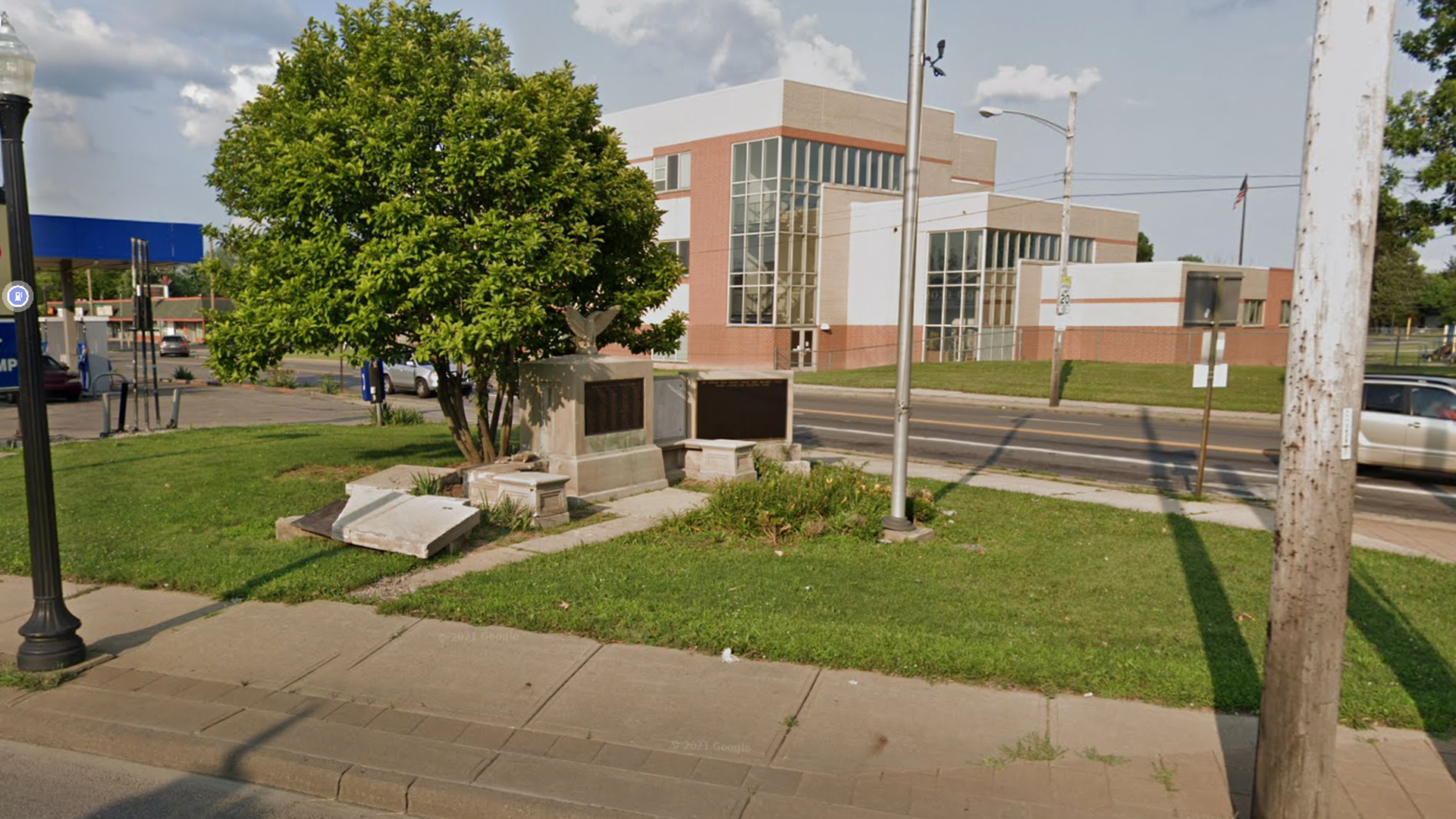 A broken monument sits at a North Linden intersection next to trees and a flagpole. 