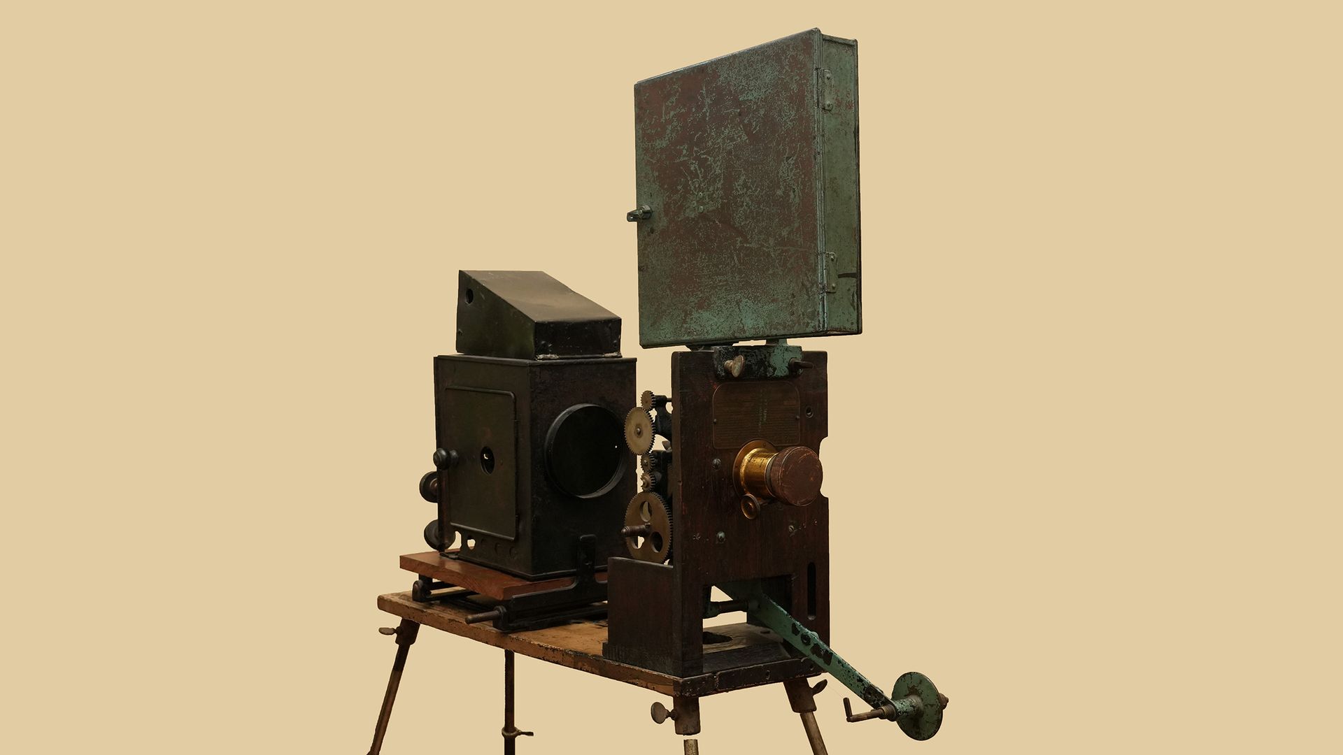 An antique machine with a tall, weathered green metal cabinet on a dark base filled with gears and levers; mounted on a wooden stand, set against a plain beige background.