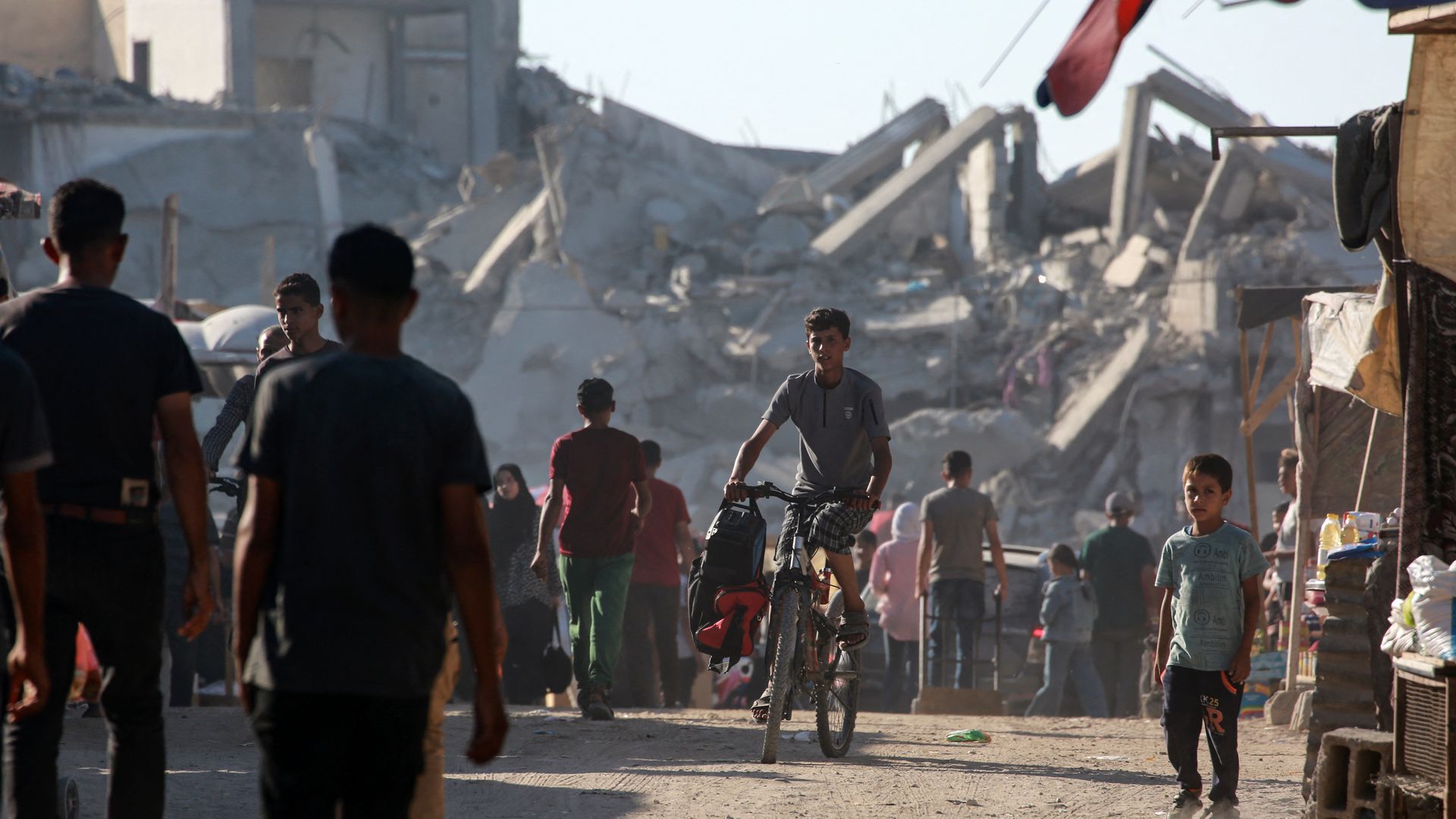 Palestinians gather at a makeshift market set up along a street devastated by Israeli bombardment in the town of Bani Suhayla near Khan Yunis in the southern Gaza Strip on July 17, 2024, amid the ongoing conflict between Israel and the Palestinian militant group Hamas. (Photo by Bashar TALEB / AFP) 