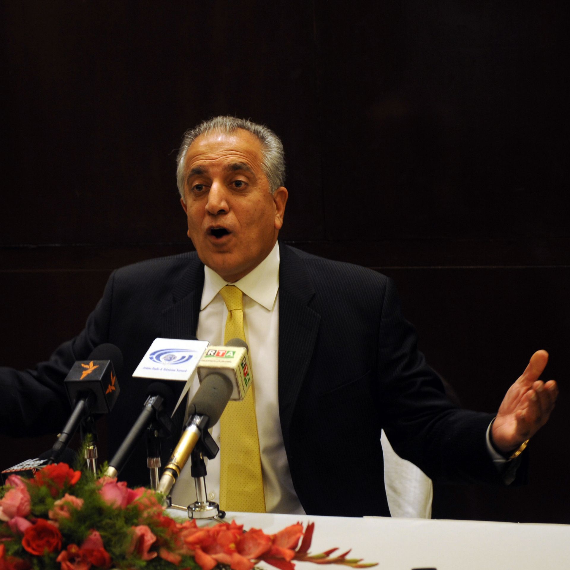 Zalmay Khalilzad speaks and gestures from a table with mics
