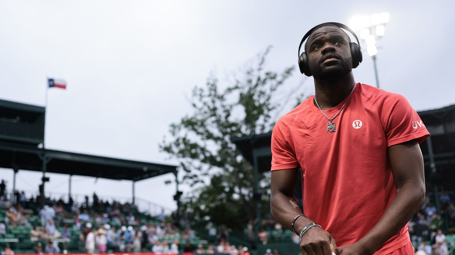 Frances Tiafoe on a tennis court wearing a red Lululemon shirt