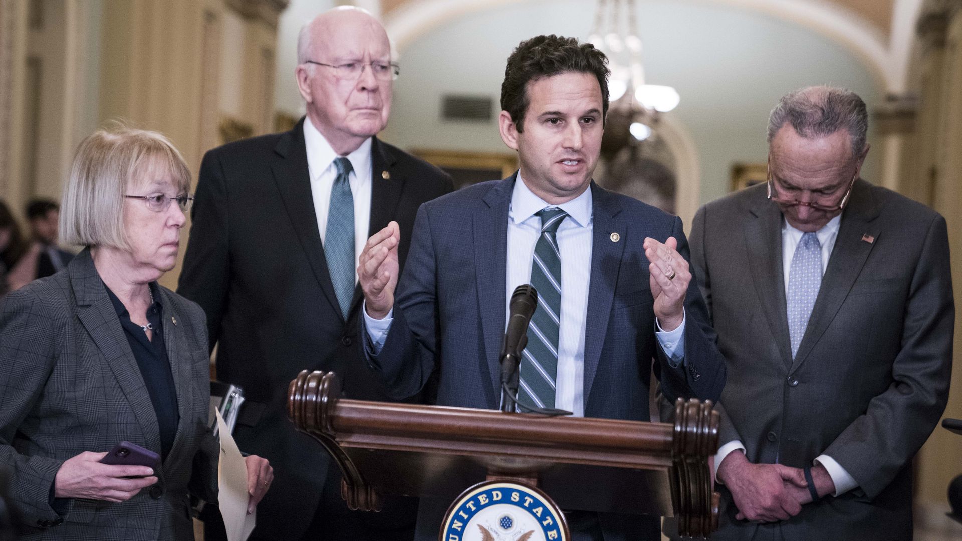 Sen. Brian Schatz of Hawaii is seen addressing reporters from a podium.