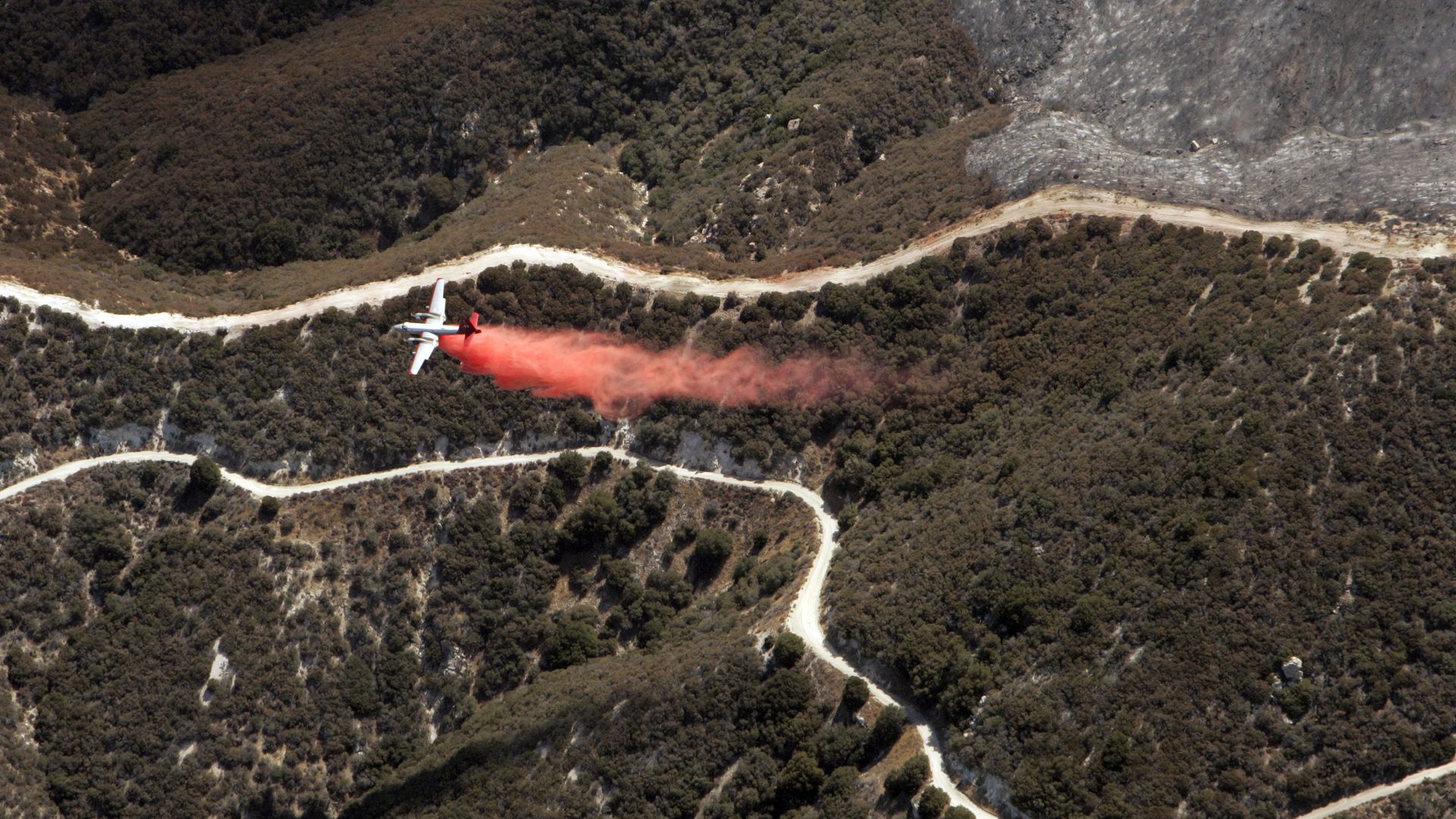 A plane dropping a chemical during a wildfire.