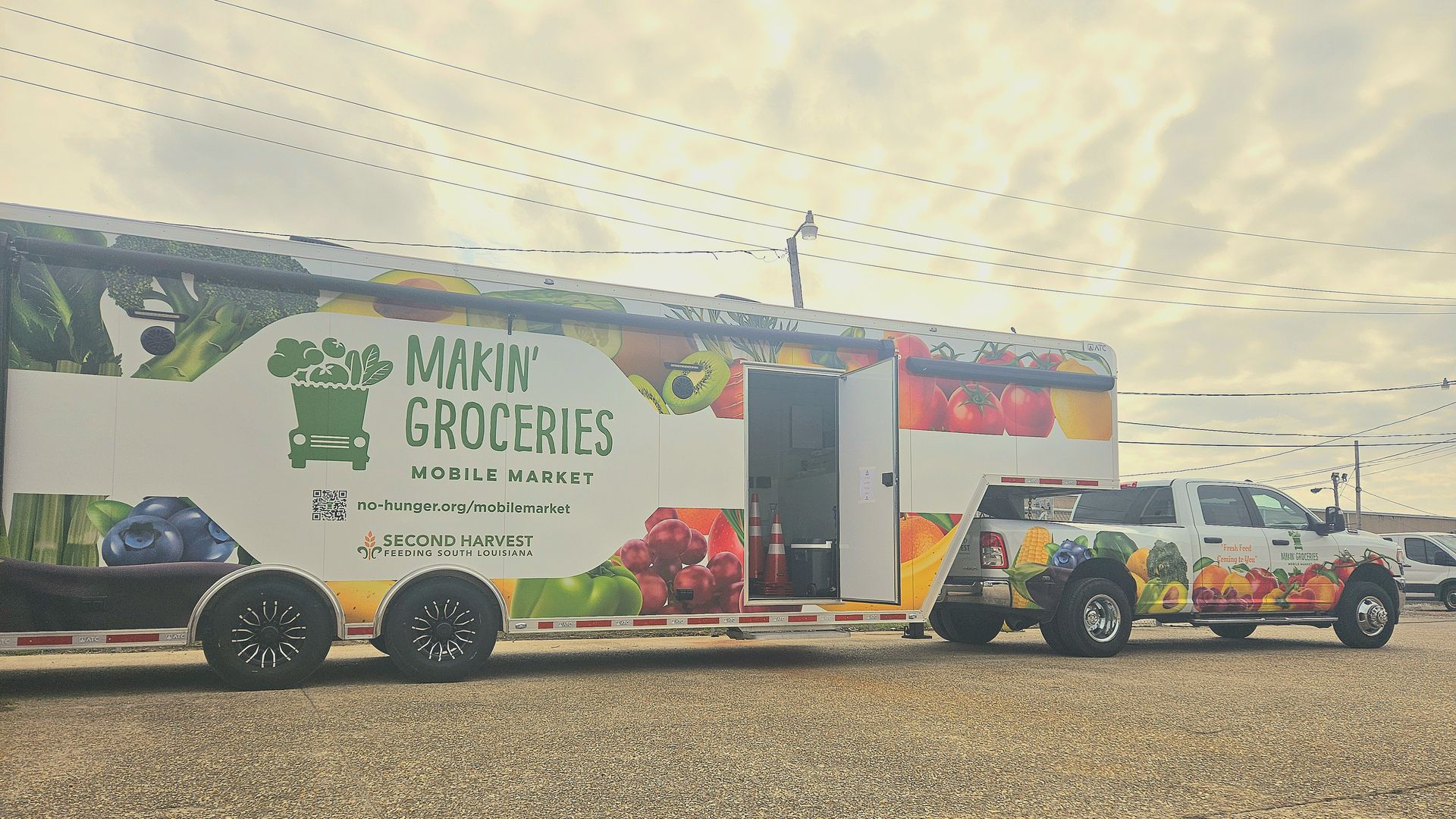 A photo of a pick-up truck pulling a long trailer that has a logo that says "Makin' groceries" with pictures of fresh produce on it.
