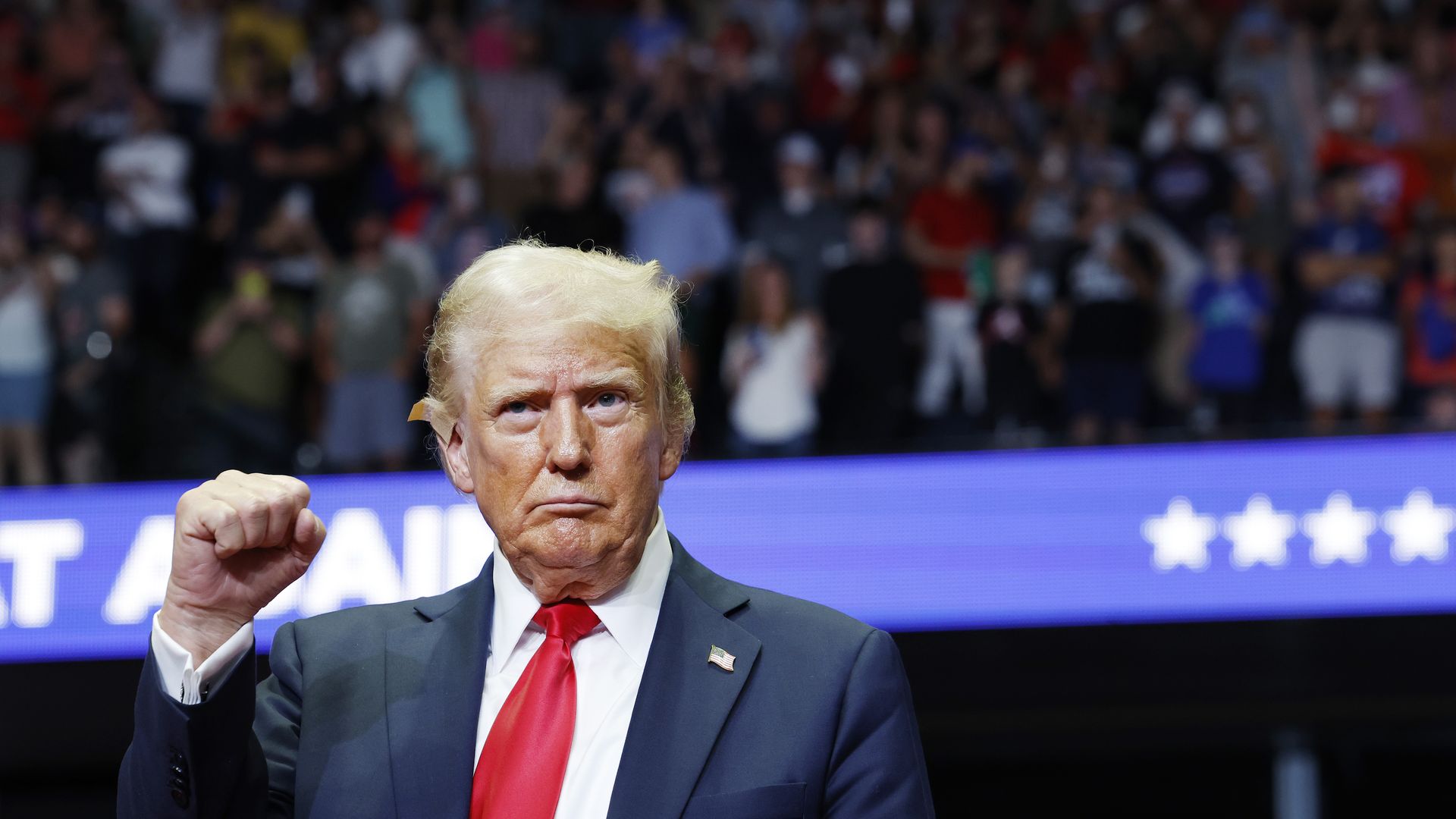 Donald Trump pumps his fist while wearing a tan bandage on his right ear.