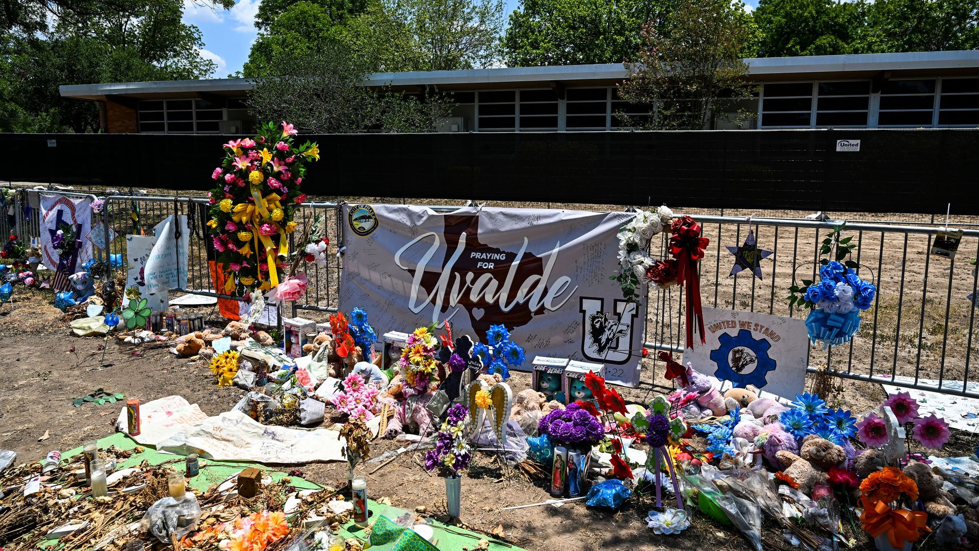 A memorial filled with flowers and teddy bears sits at the front gate of Robb Elementary in Uvalde