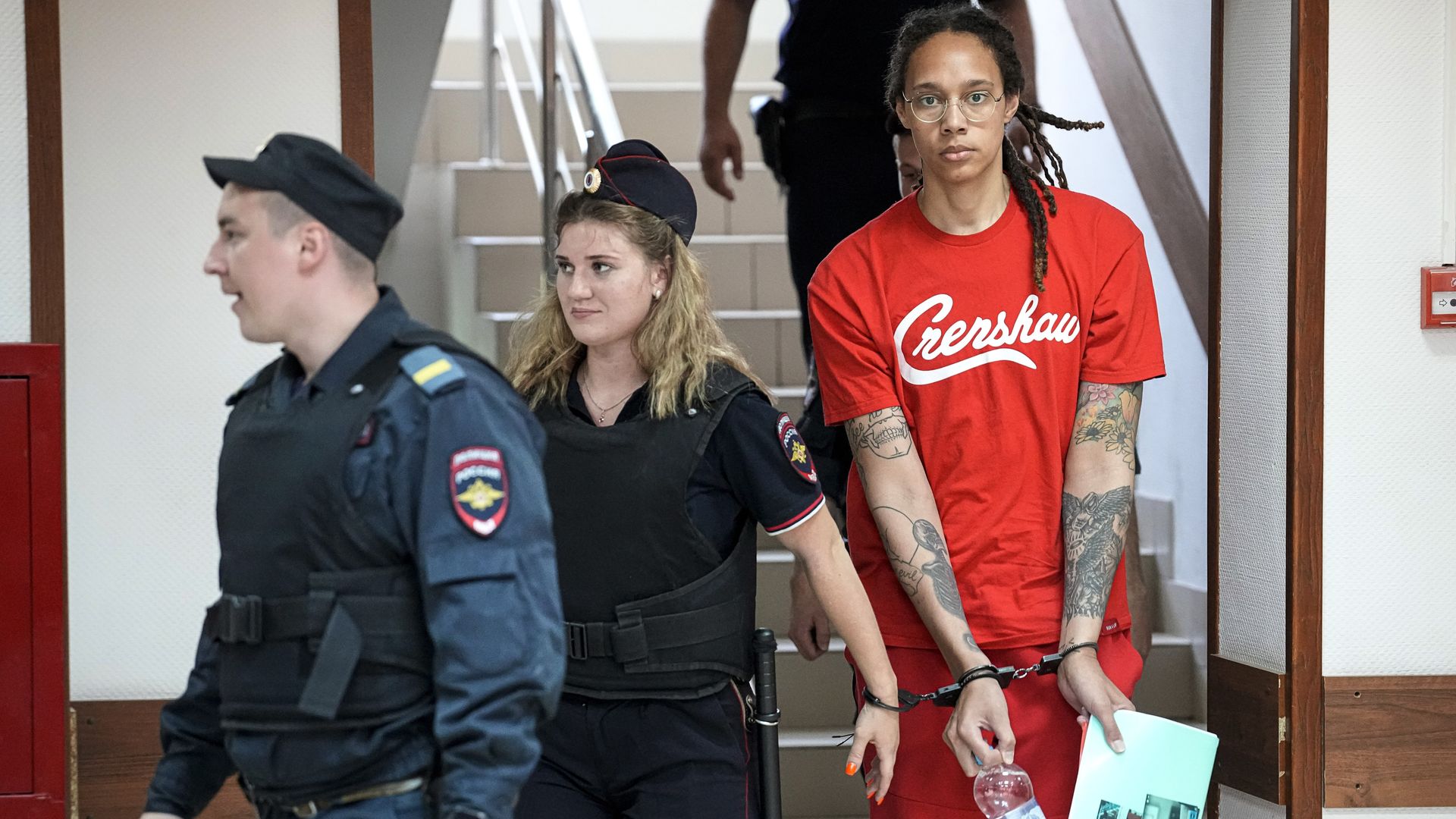 A guard escorts a woman in handcuffs.