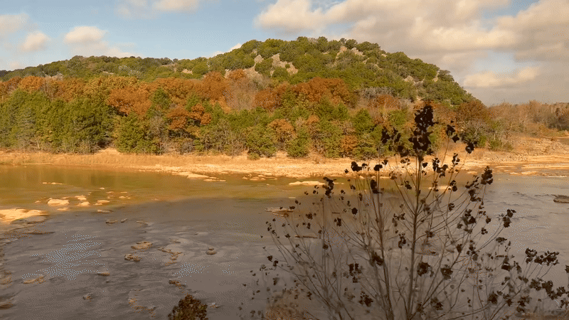 A moving gif of the view of small mountains and a river from a train