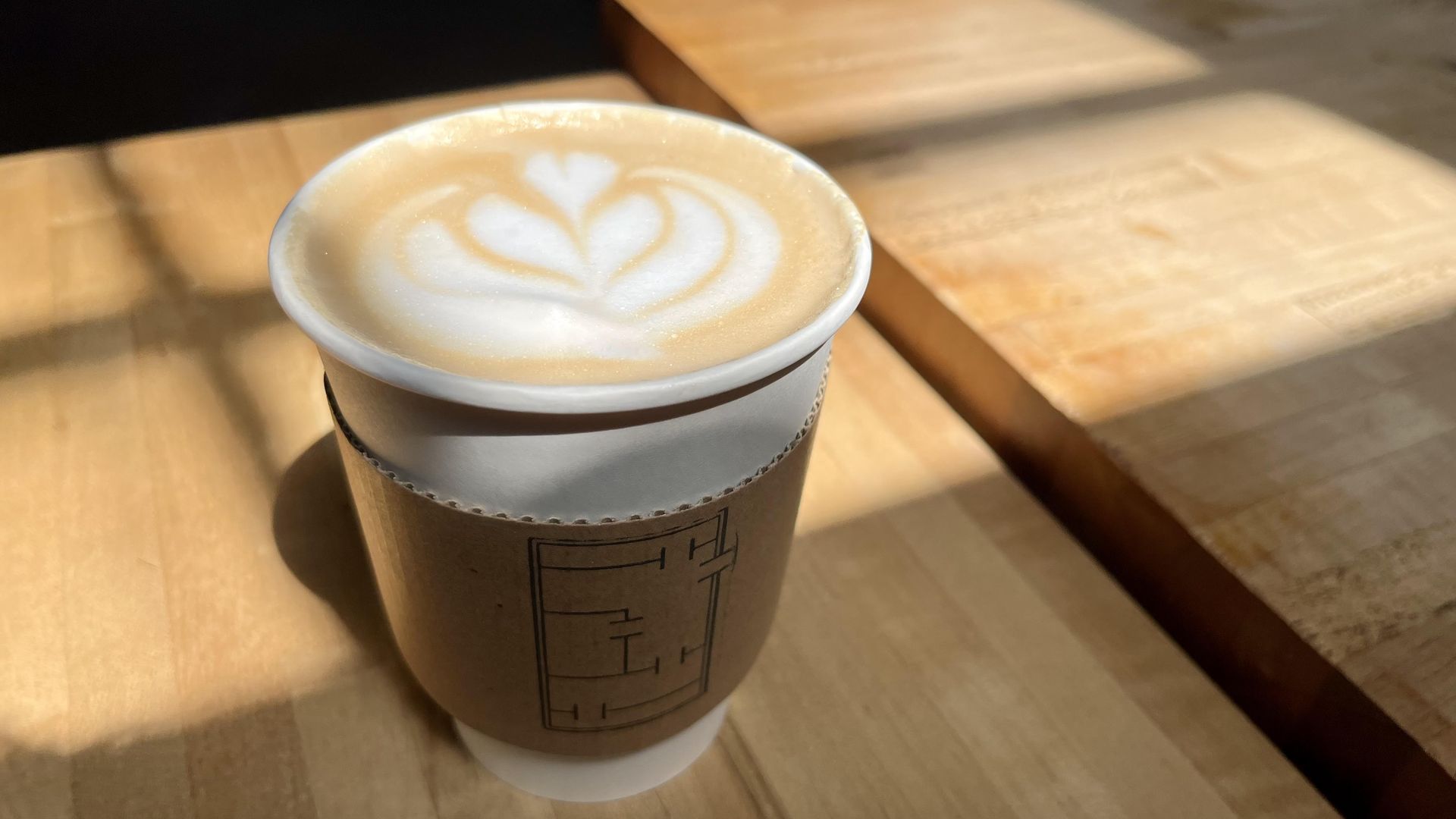 Sunlight falls on a latte on a wooden table.