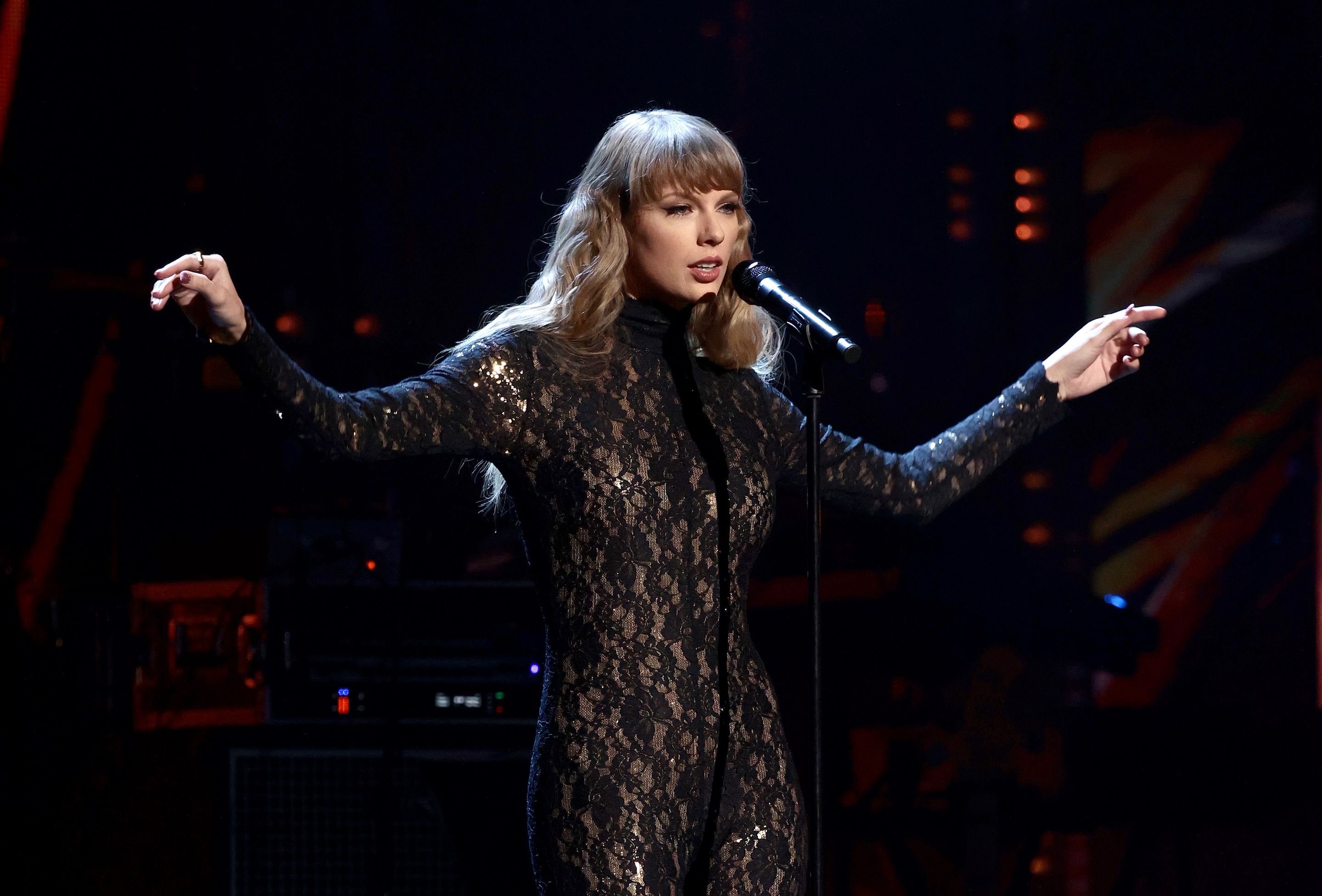 Taylor Swift performs on stage in a lace cat suit. 