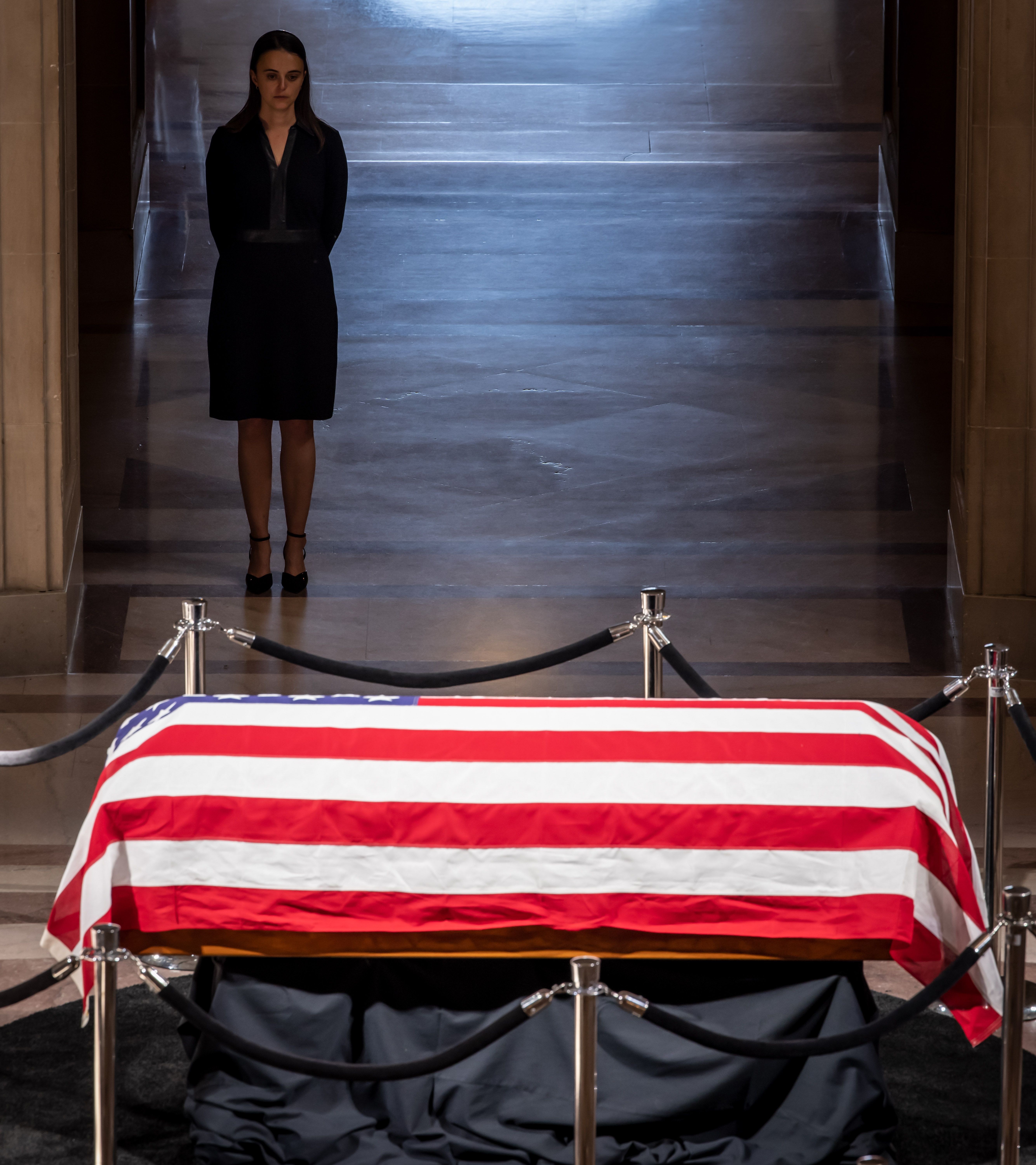 Feinstein's granddaughter stands in a dark dress overlooking the casket, which is wrapped in an American flag.