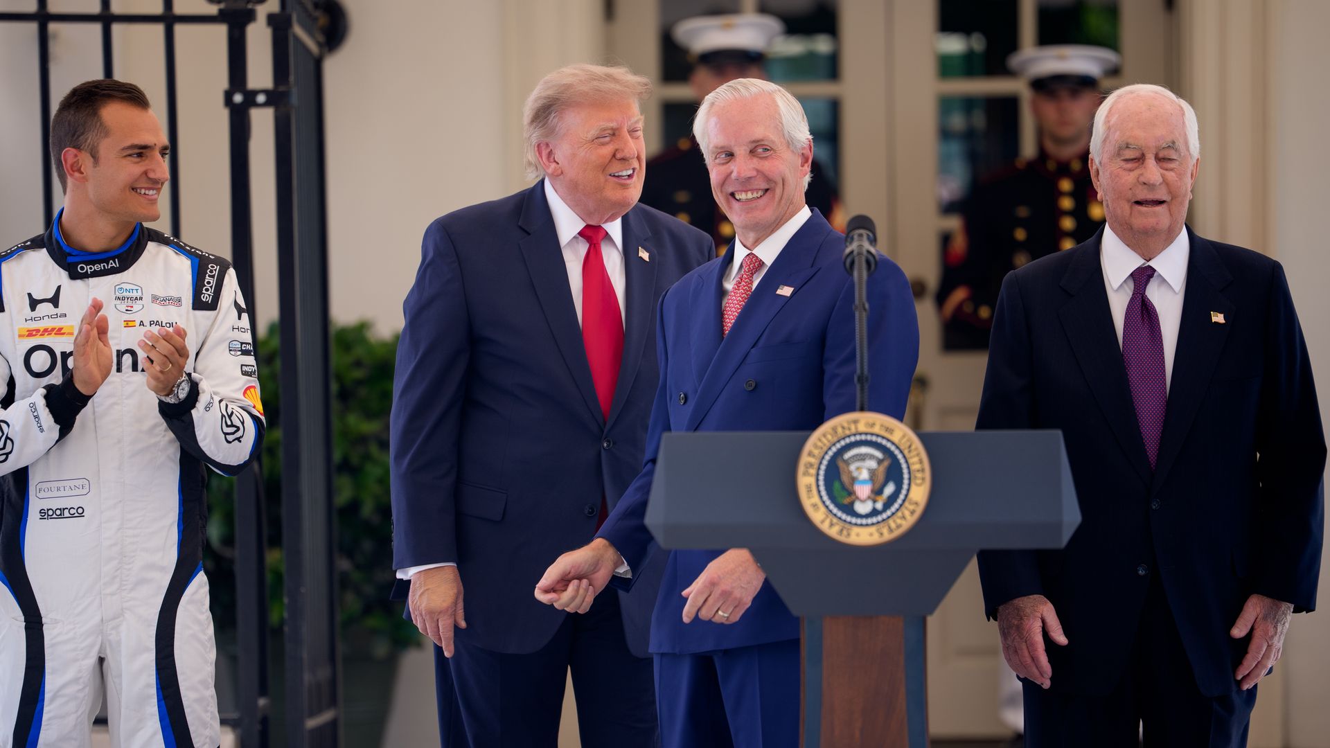 Bud Denker stands at a podium outside The White House with President Donald Trump and Roger Penske.