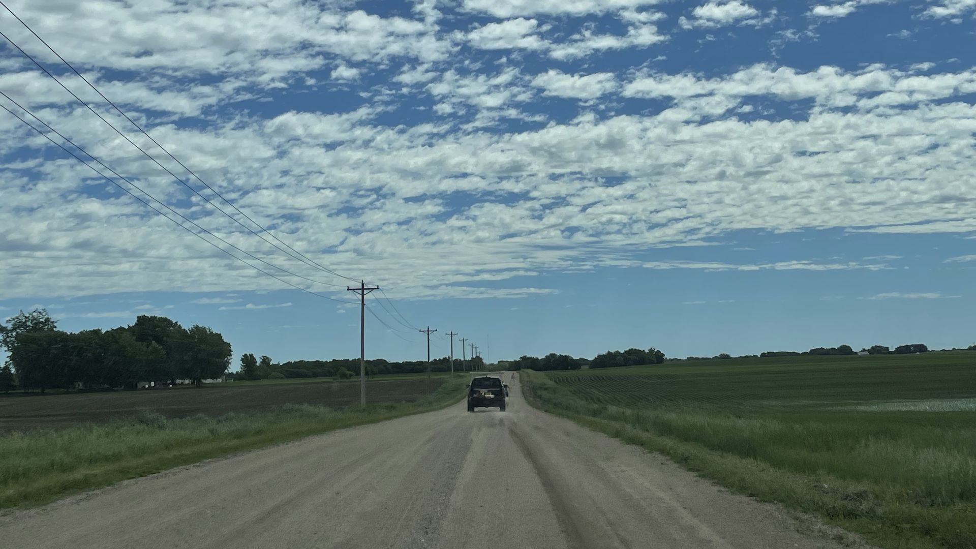 a truck on a dirt road with blue skies and clouds