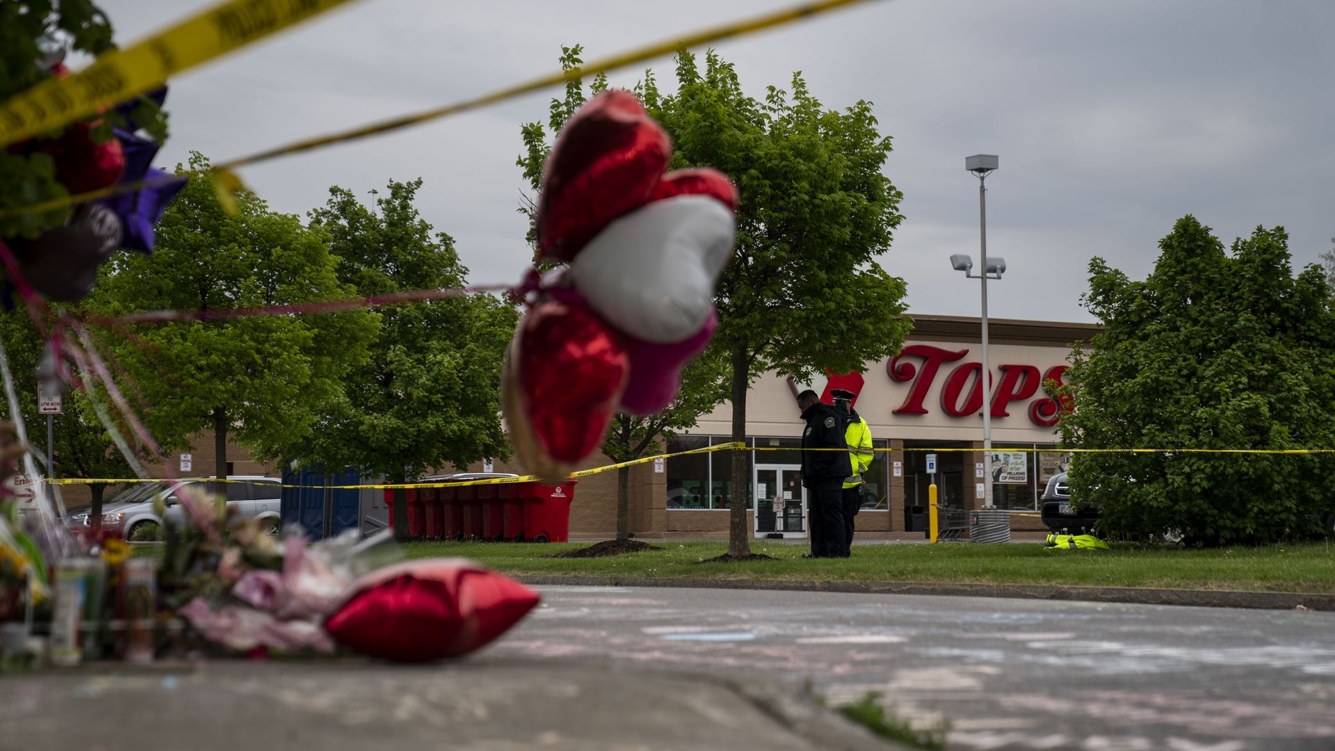 Photo of balloons and police yellow tape in the foreground with the Tops grocery store building in focus