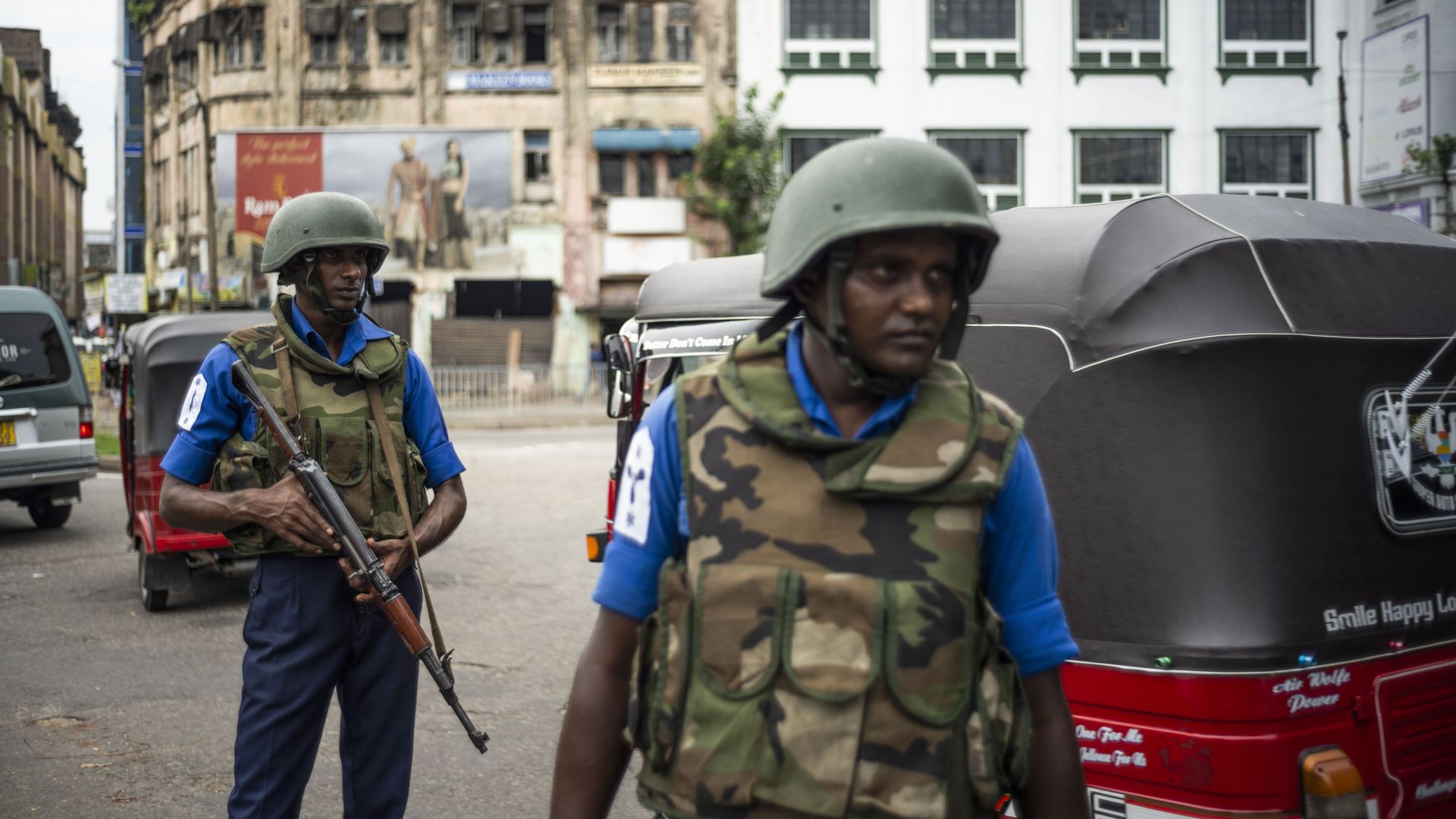 In this image, two armed and helmeted soldiers walk down the middle of the street. 
