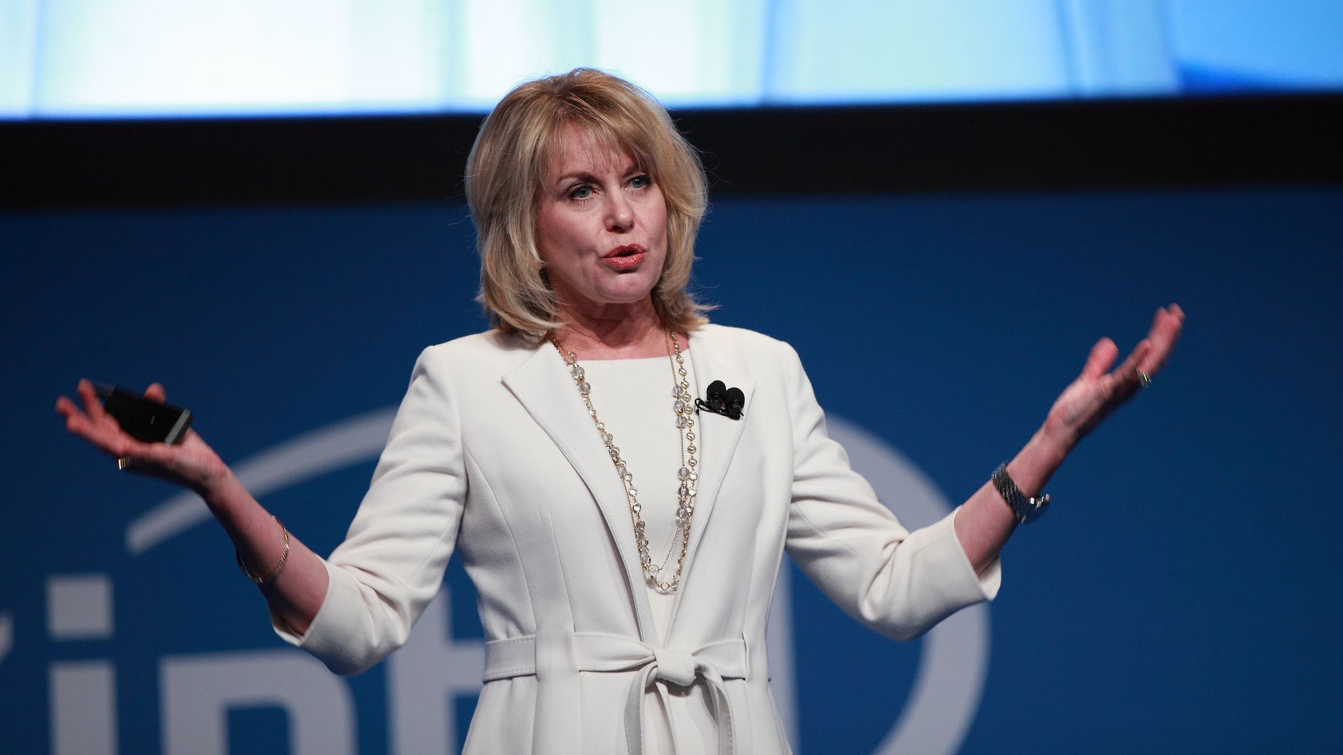 Diane Bryant in white dress on stage with phone in hand
