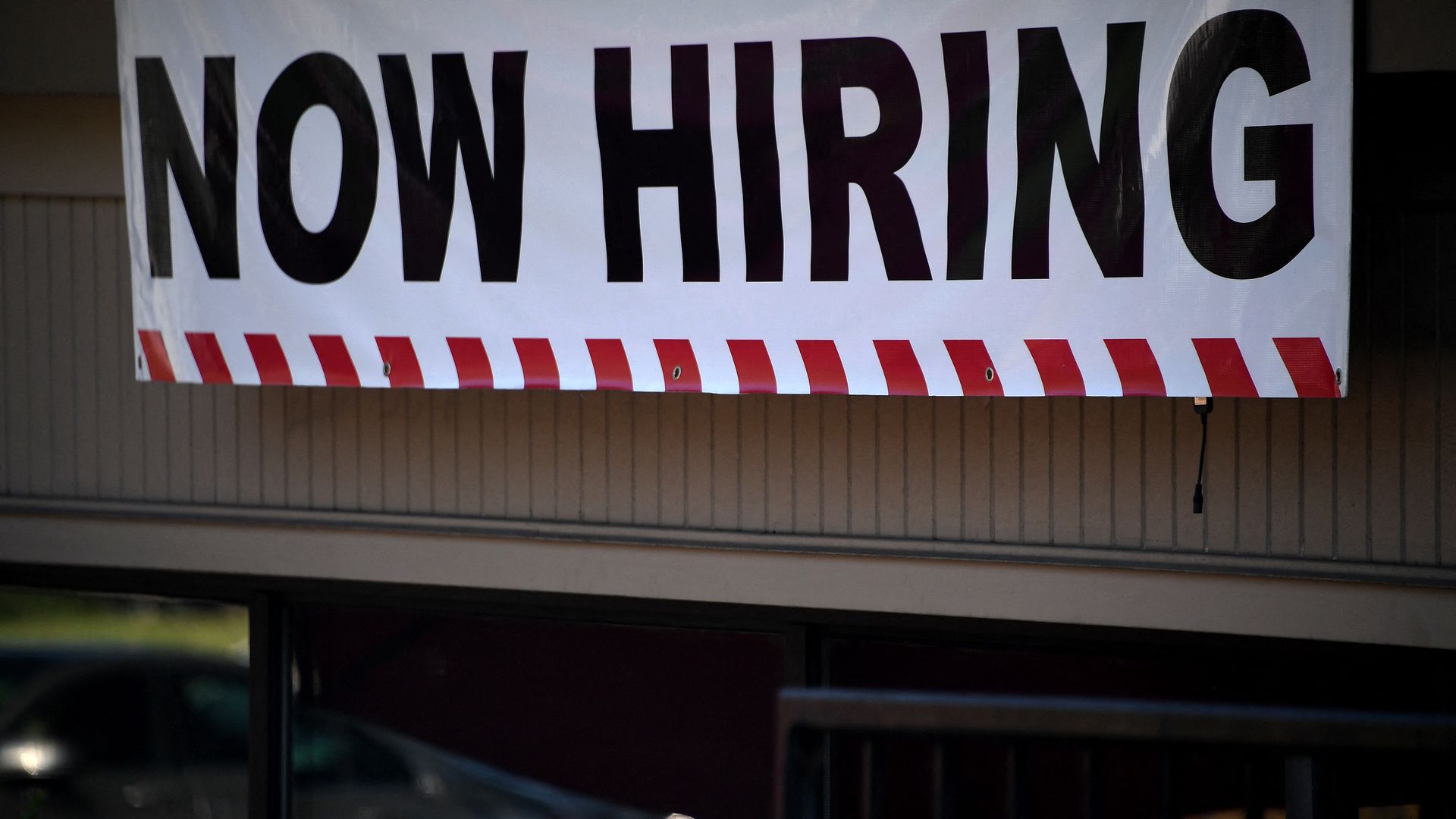 Photo of a white banner that says "Now Hiring" draped over the top of a restaurant