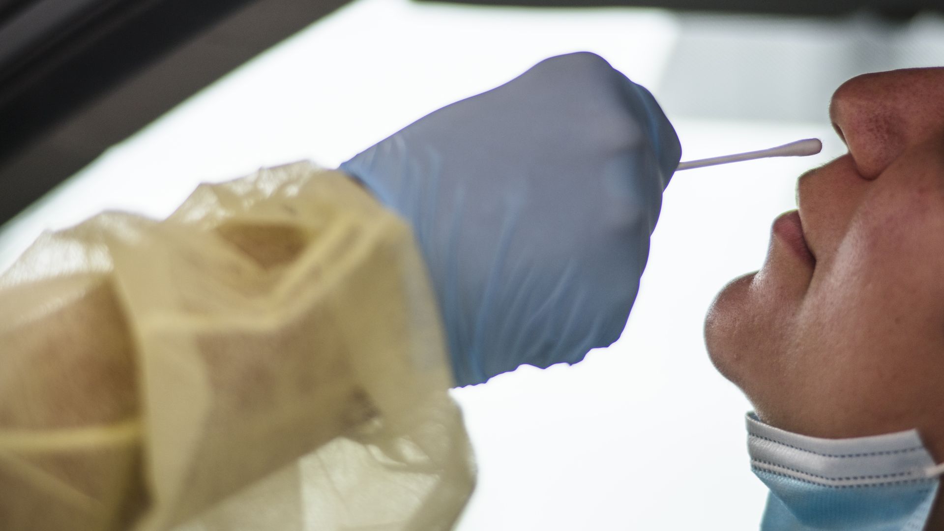 A healthcare worker prepares to swab a person's nose for COVID.