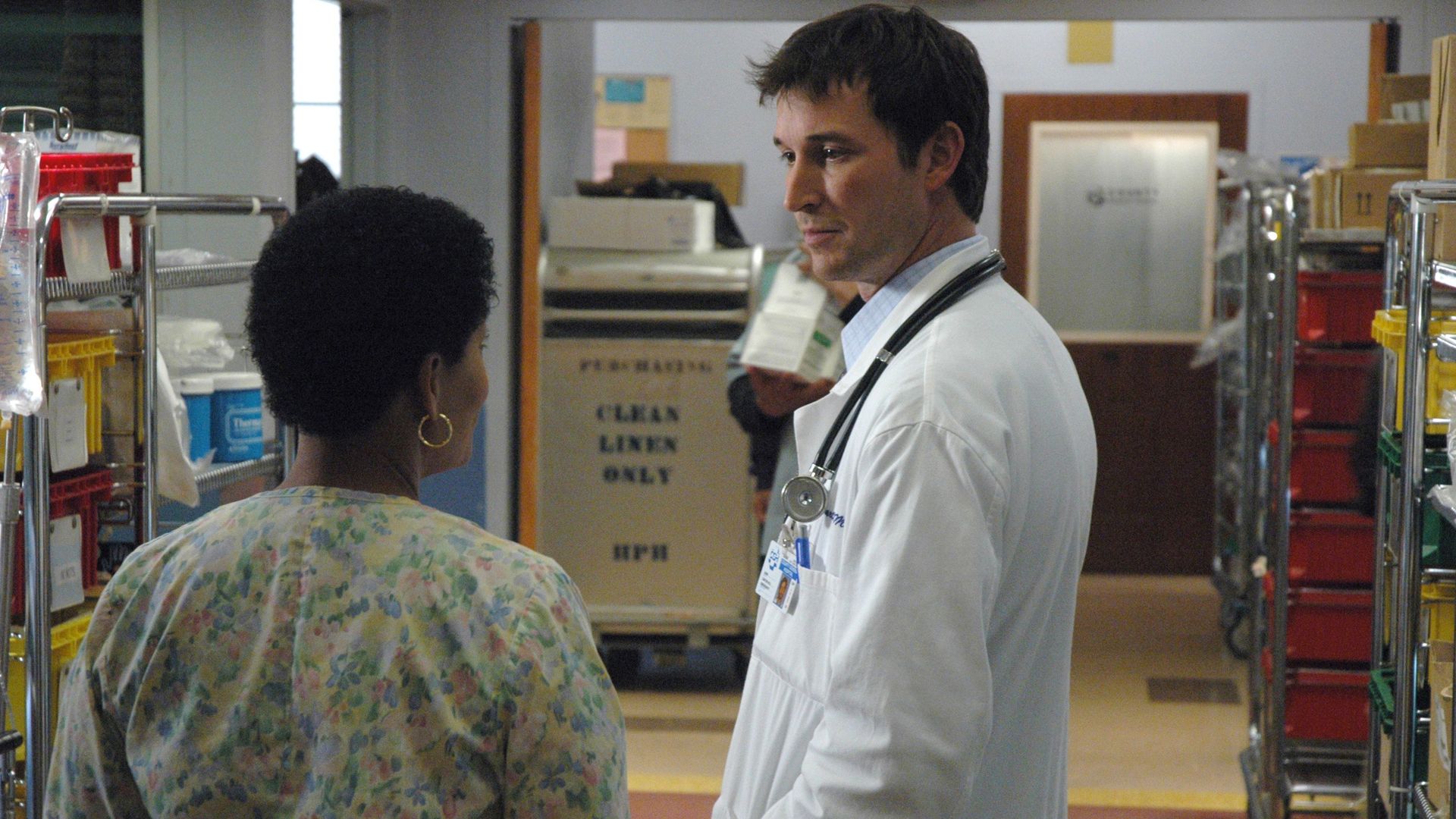 A person in a white lab coat speaks to a person in a nurse's shirt