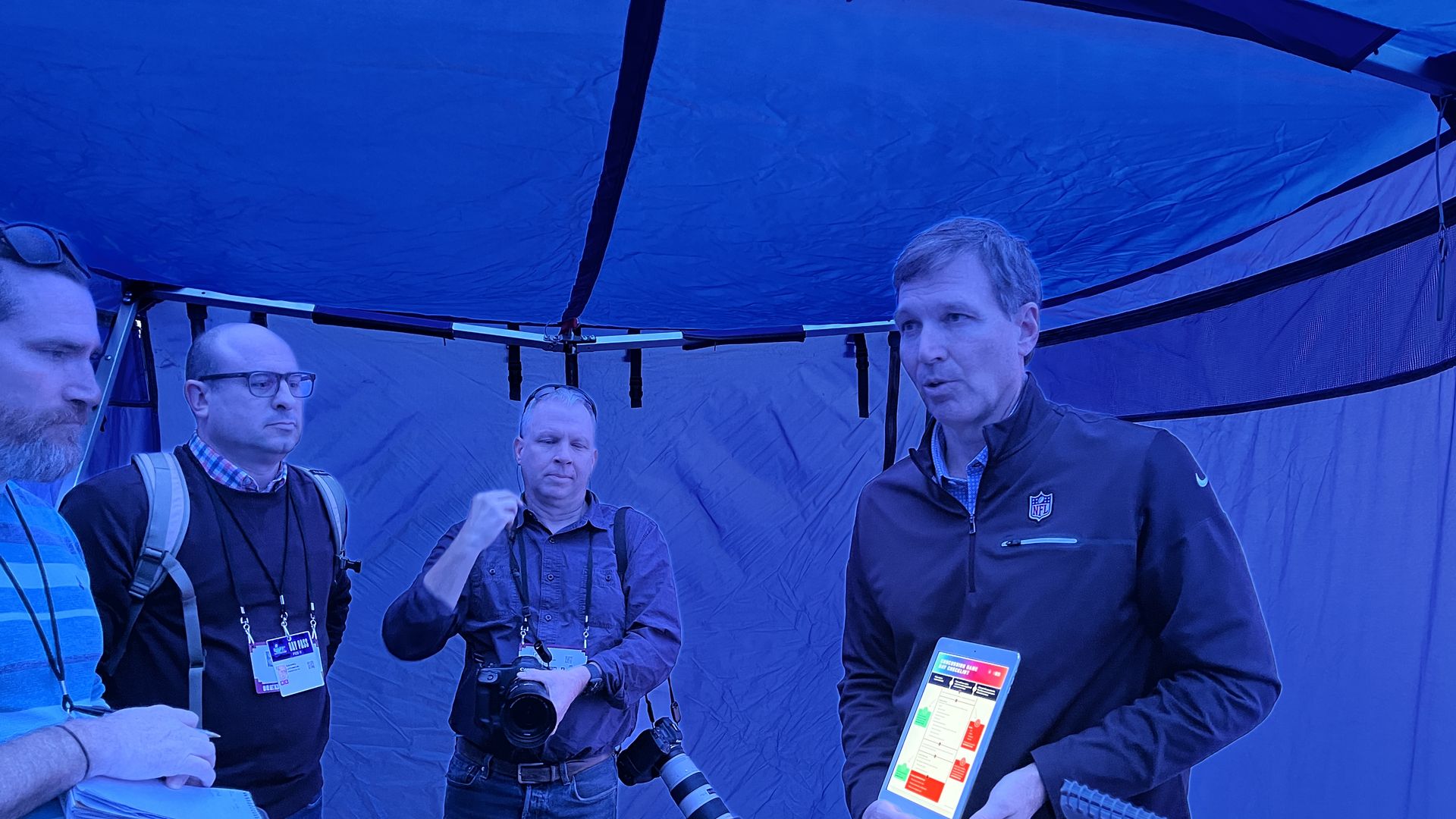A man holds an ipad inside a blue tent.