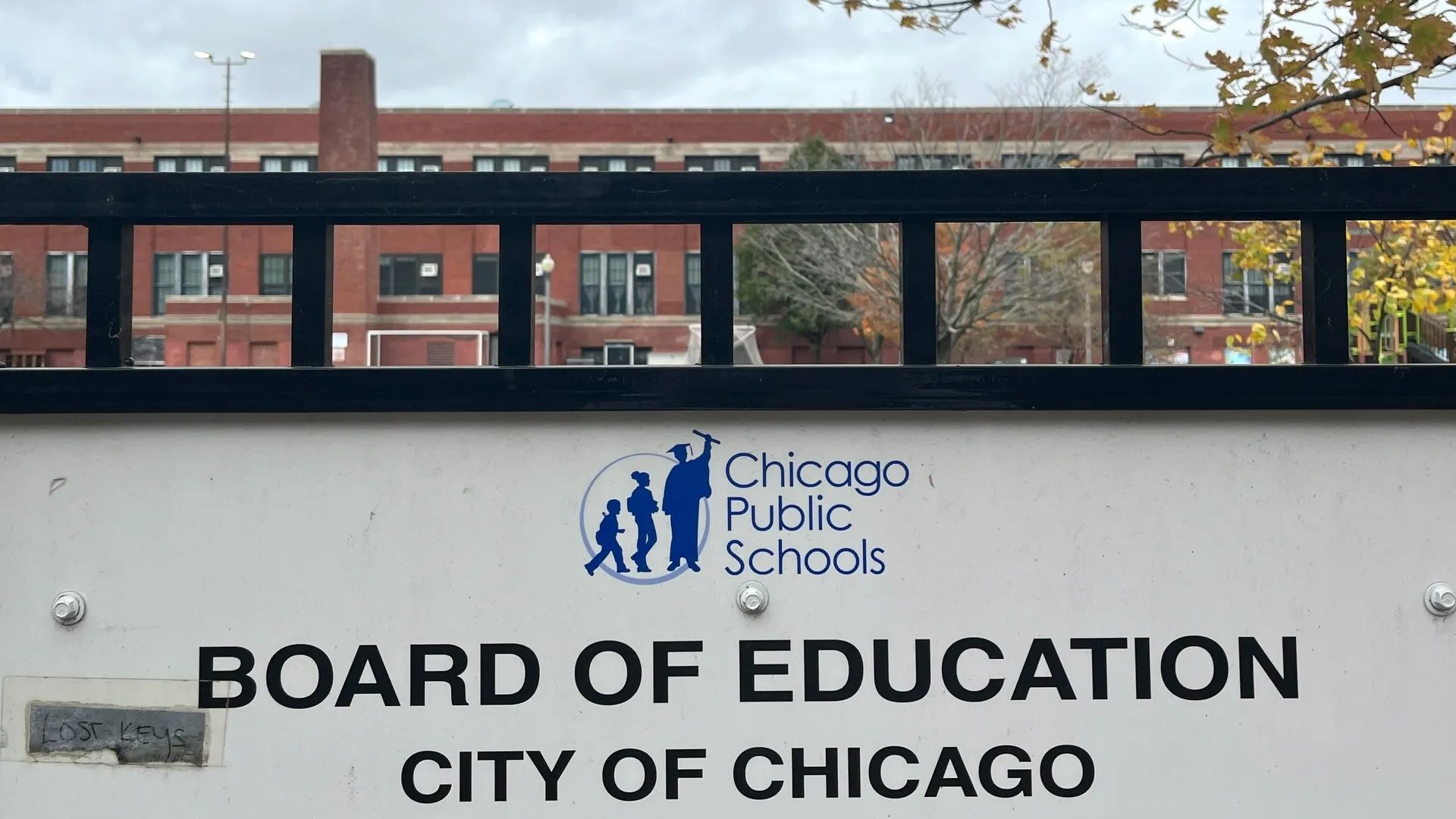 White sign "Chicago Board of Education City of Chicago" on a black fence in front of a school.
