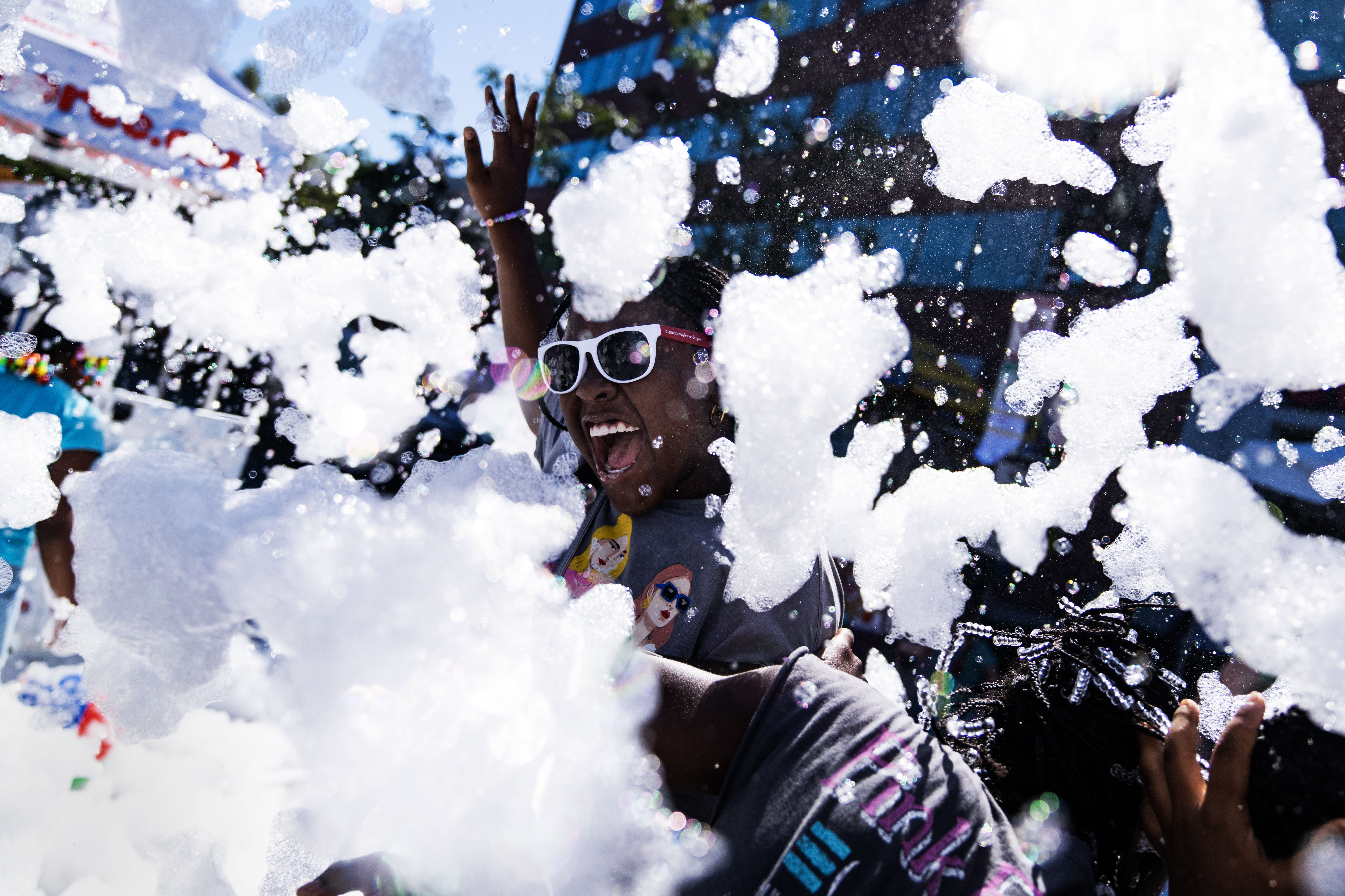 A kid in sunglasses smiles as they play in foam at H Street Festival