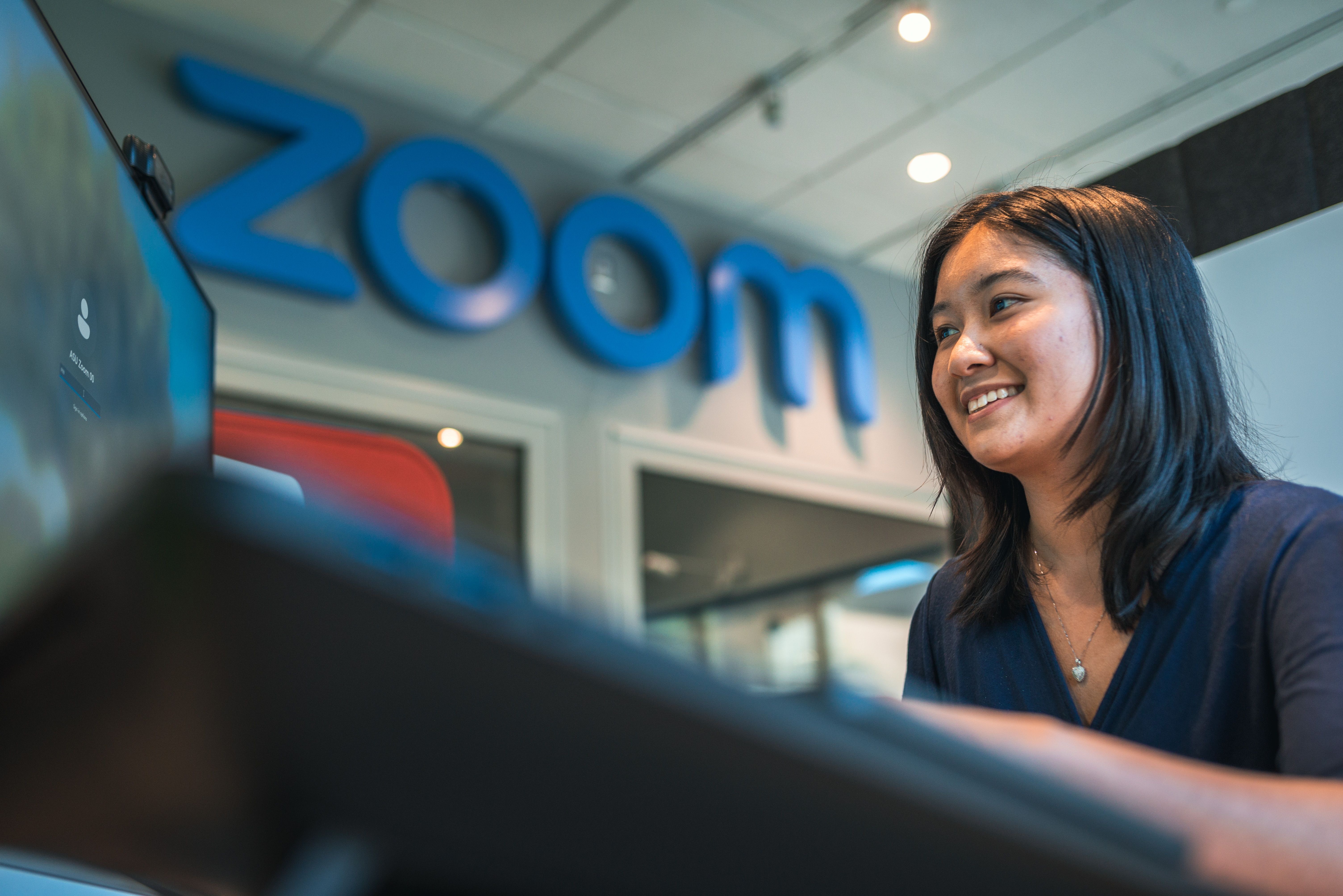 A woman at a computer under a sign that says Zoom. 